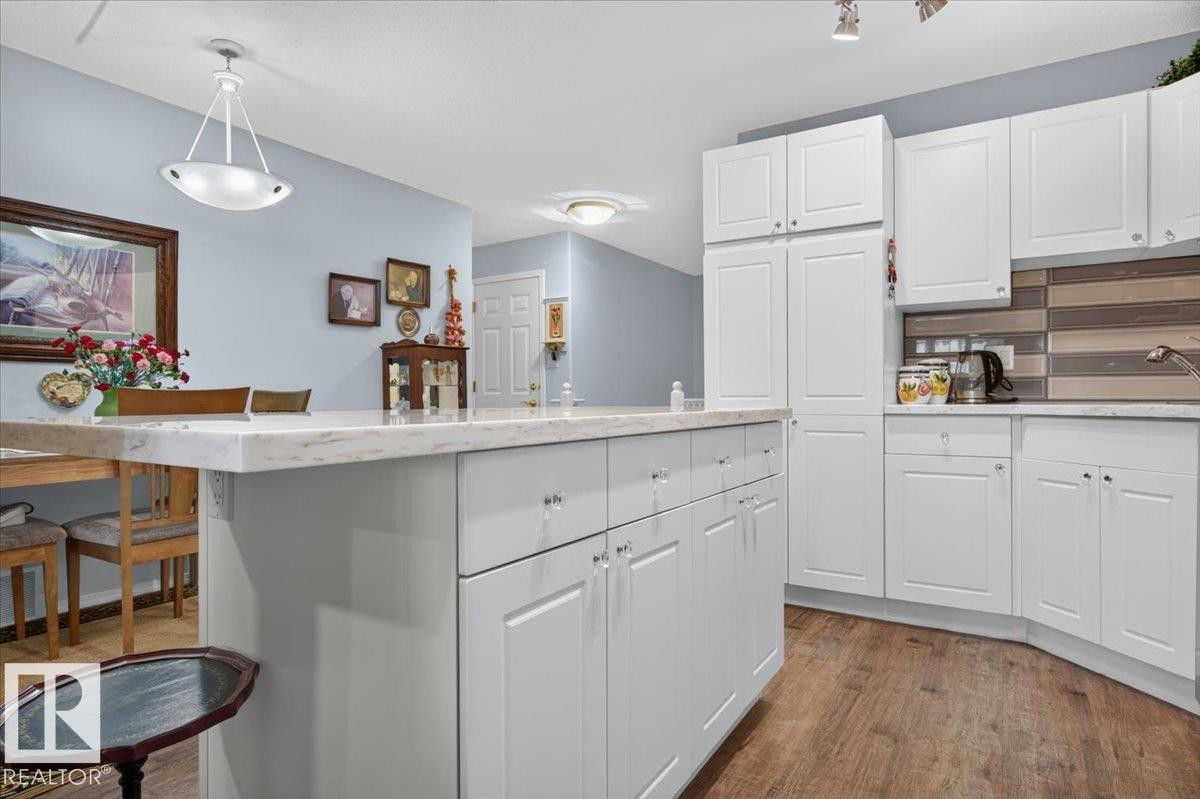 Kitchen with white cabinetry, wood-finish flooring, a light-toned countertop, and a tiled backsplash - #125 4610 50 Ave, Stony Plain, AB