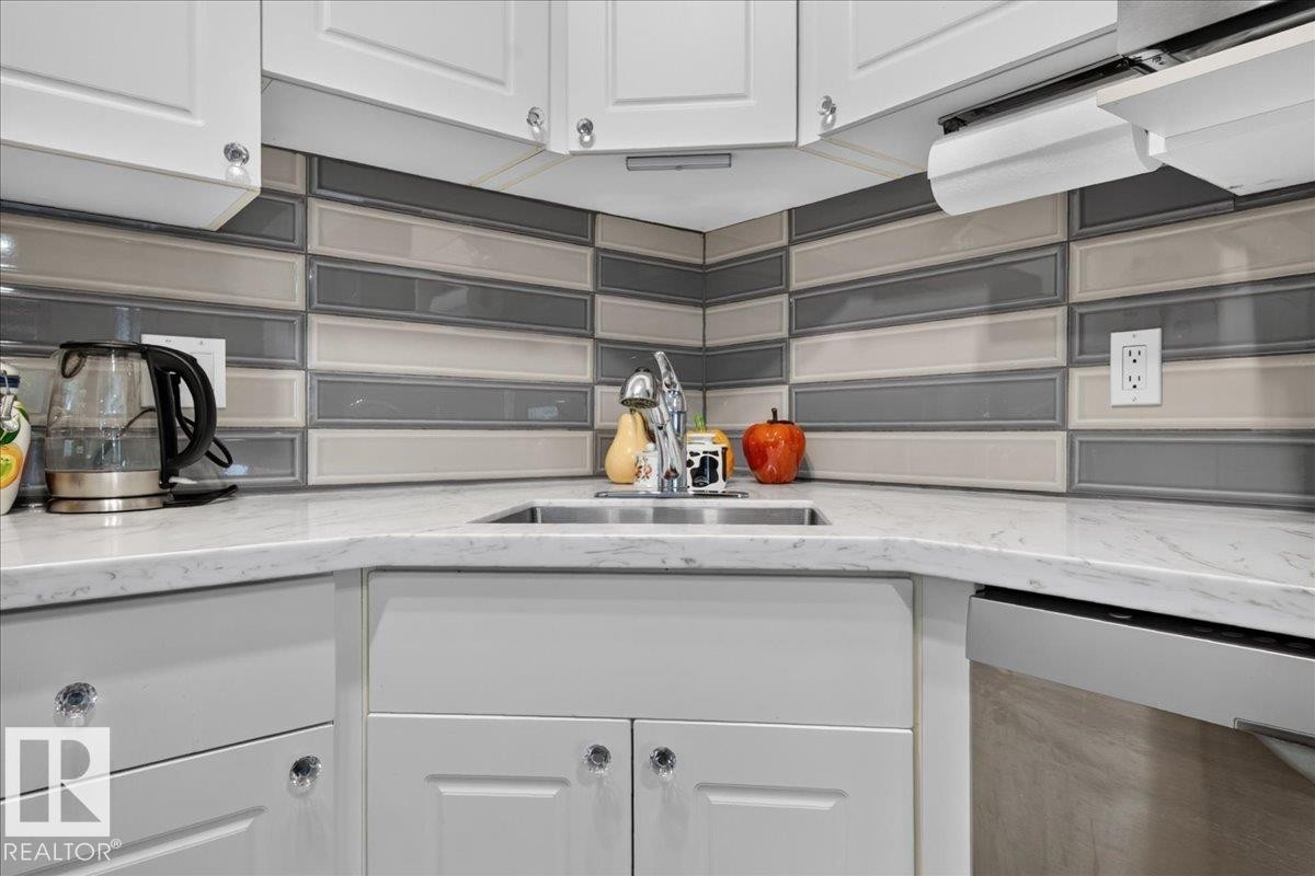 White cabinetry with crystal knobs, stainless steel undermount sink, solid surface countertops, and a multi-tone tile backsplash - #125 4610 50 Ave, Stony Plain, AB