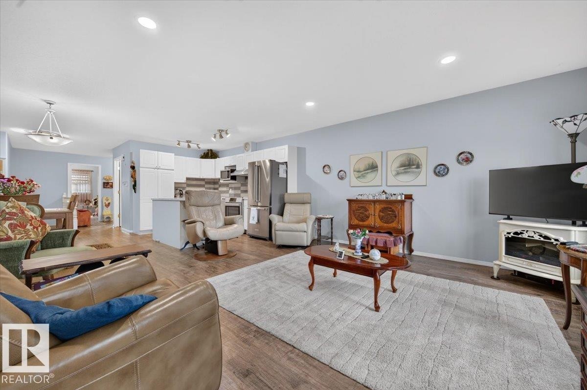 Wood-finish flooring throughout, recessed lighting, and a modern kitchen with white cabinetry - #125 4610 50 Ave, Stony Plain, AB