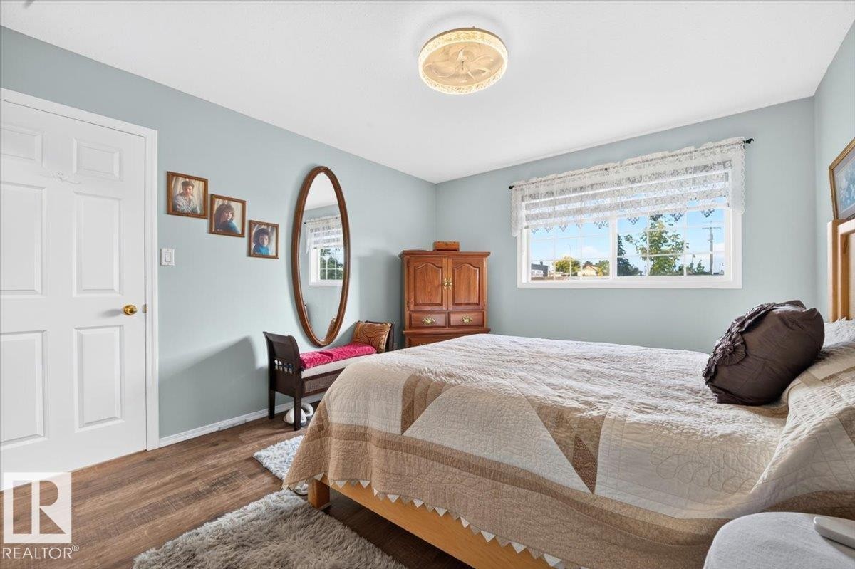 Wood-finish flooring, light blue wall paint, a white paneled door, and a single window with white trim - #125 4610 50 Ave, Stony Plain, AB
