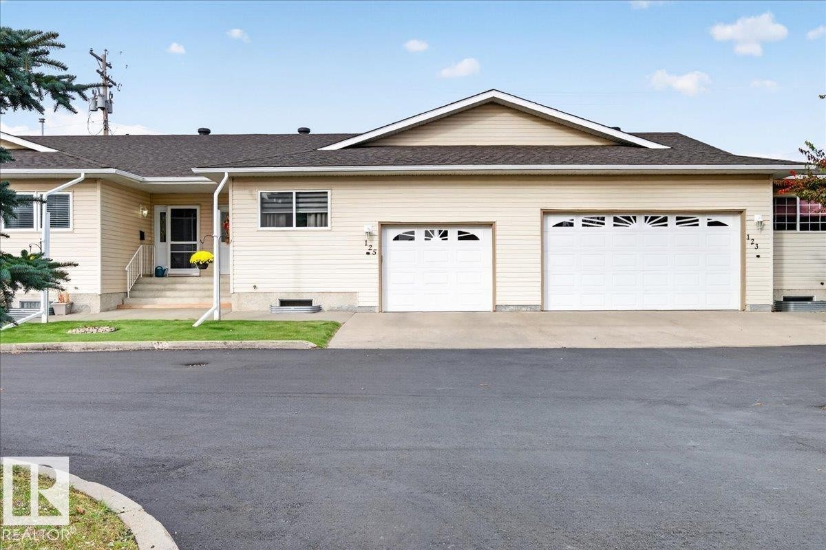 Siding exterior with multiple windows, two-car garage, and concrete entry steps - #125 4610 50 Ave, Stony Plain, AB