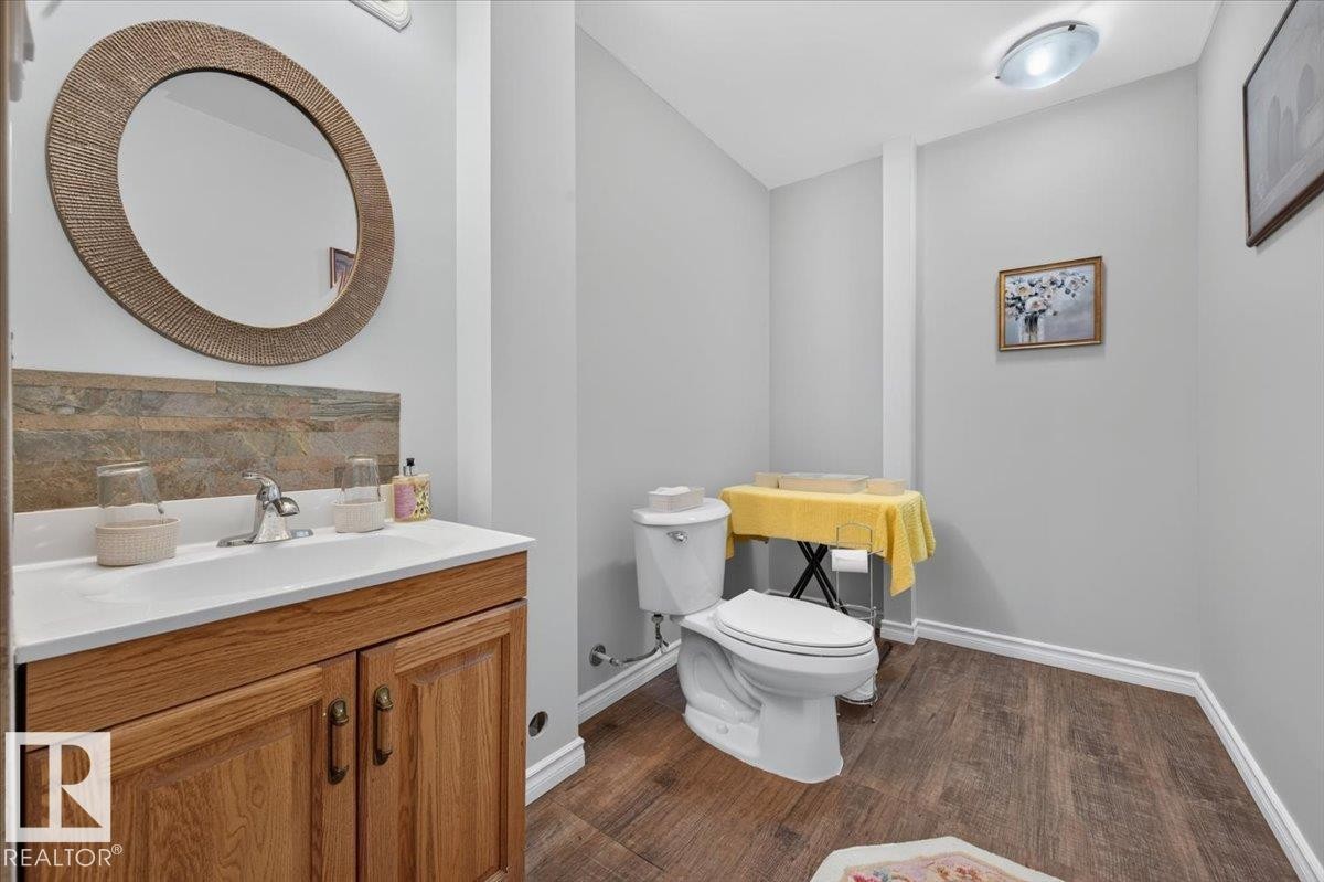 Wood-finish flooring, vanity with wood-finish cabinetry, white countertop, and stone-look backsplash - #125 4610 50 Ave, Stony Plain, AB