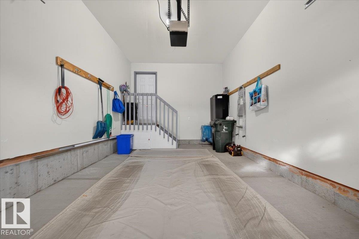 Spacious garage with concrete flooring, painted walls, and a built-in staircase - #125 4610 50 Ave, Stony Plain, AB