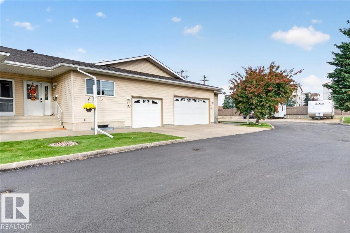 Two-car attached garage, paved driveway, mature trees, manicured lawn, and exterior siding - #125 4610 50 Ave, Stony Plain, AB