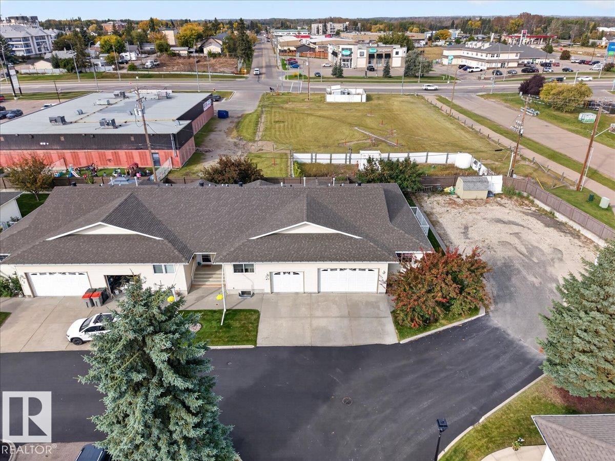 Duplex property with asphalt shingle roofing, attached garages, concrete driveways, and manicured landscaping - #125 4610 50 Ave, Stony Plain, AB