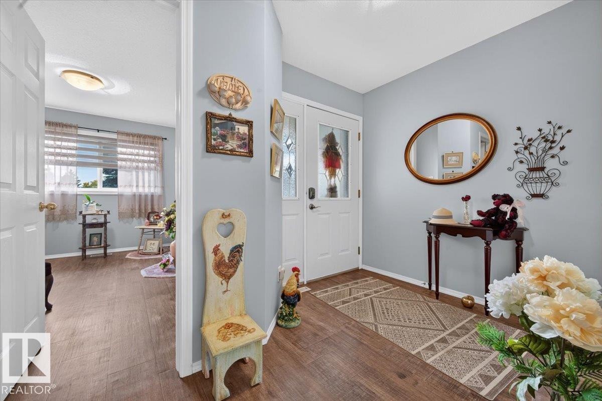 Light gray wall paint, wood-finish flooring, white interior doors, and a front entry door with decorative glass inserts - #125 4610 50 Ave, Stony Plain, AB