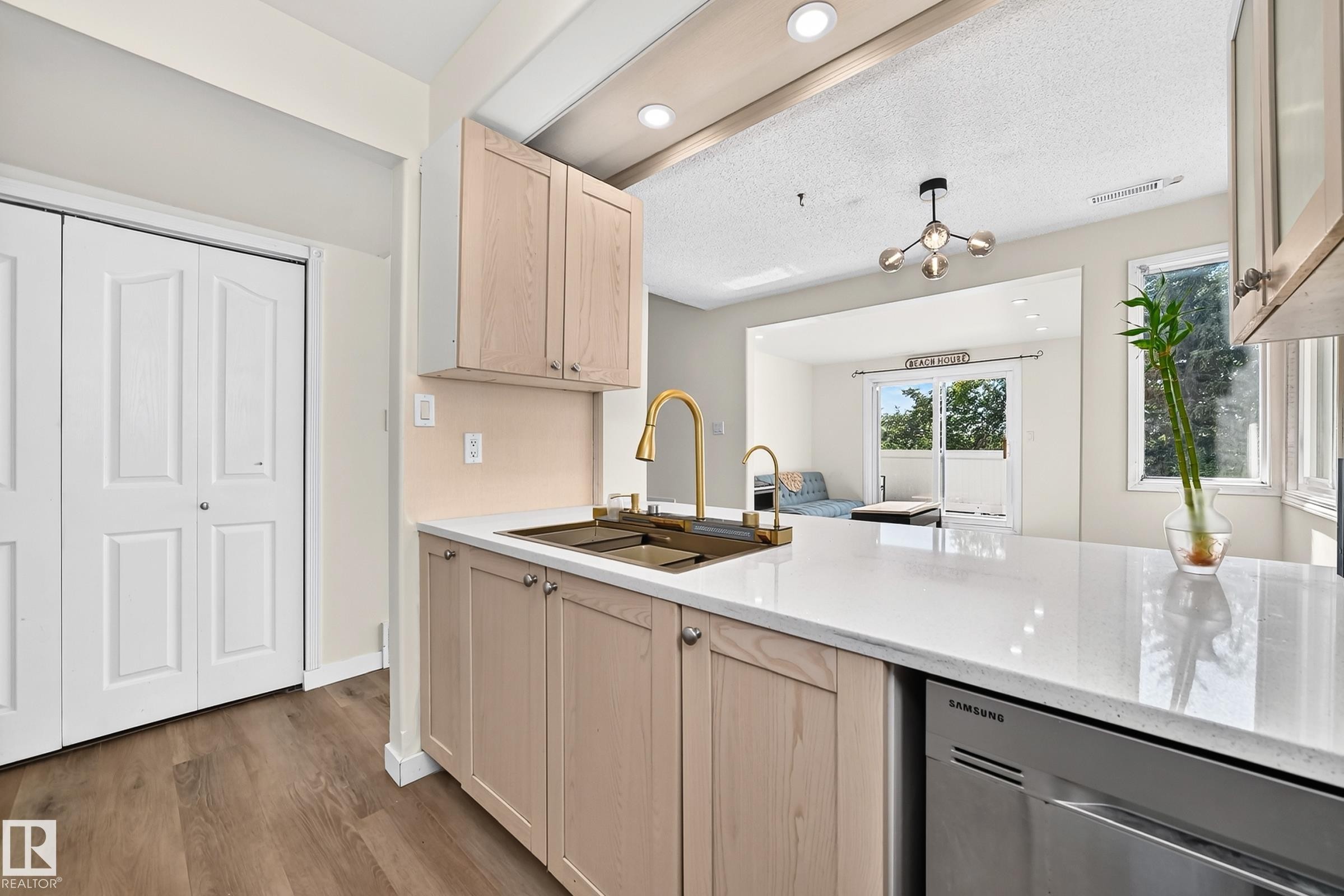 Contemporary kitchen featuring warm wood-finish cabinetry, white quartz countertops, a center island with seating space, stainless steel appliances, and a brass pull-down faucet - 161 Lancaster Terrace Nw, Edmonton, AB
