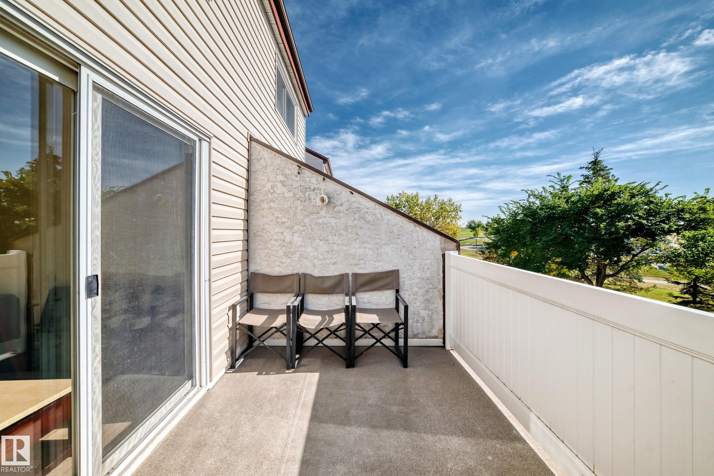 Private balcony with a sliding glass door, textured exterior wall, and white panel fencing - 161 Lancaster Terrace Nw, Edmonton, AB