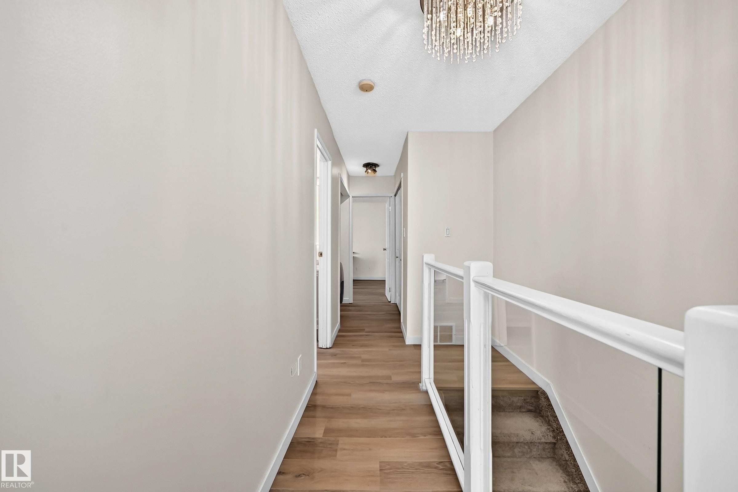 Hallway featuring wood-finish flooring, light neutral paint, and white trim - 161 Lancaster Terrace Nw, Edmonton, AB