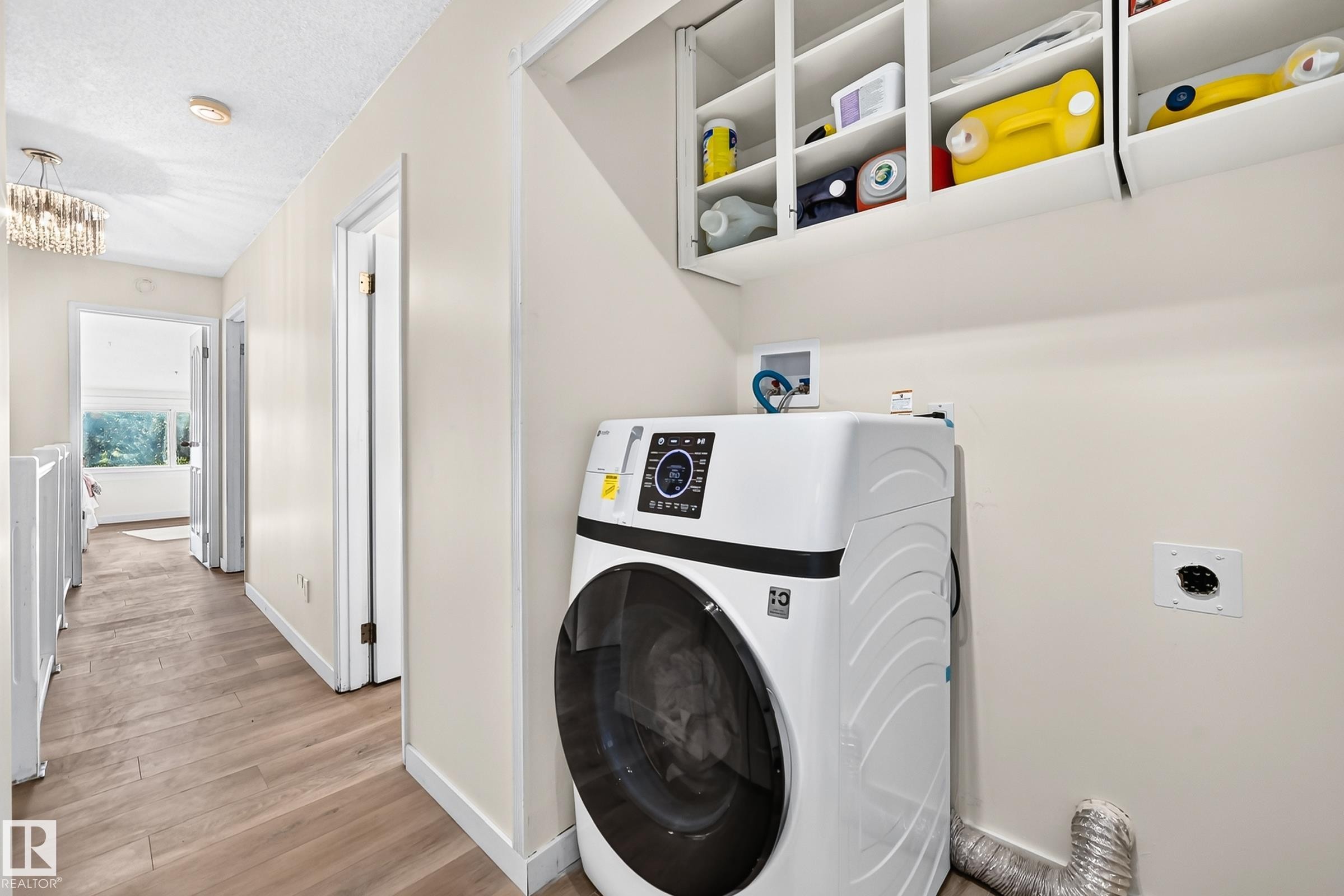 Hallway laundry area featuring a front-load appliance, integrated wall cabinetry, and wood-finish flooring - 161 Lancaster Terrace Nw, Edmonton, AB