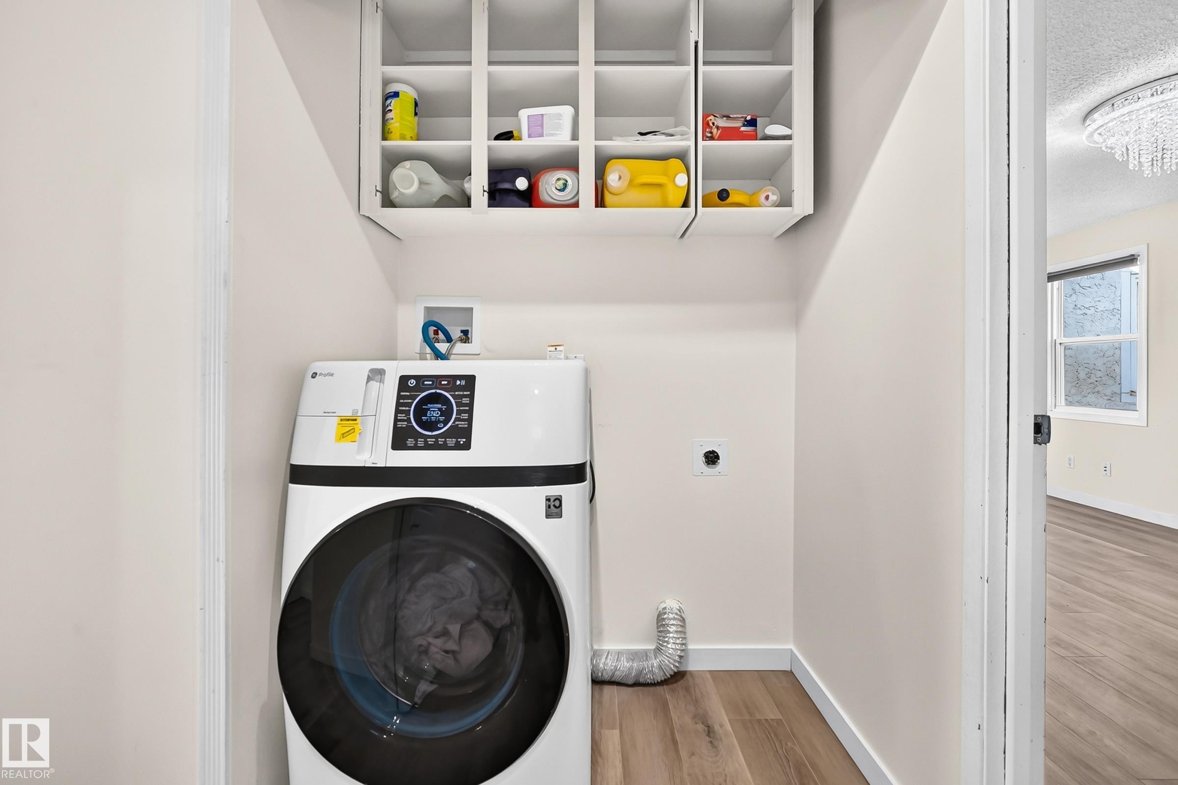 Dedicated laundry area with upper white cabinetry and wood-finish flooring - 161 Lancaster Terrace Nw, Edmonton, AB