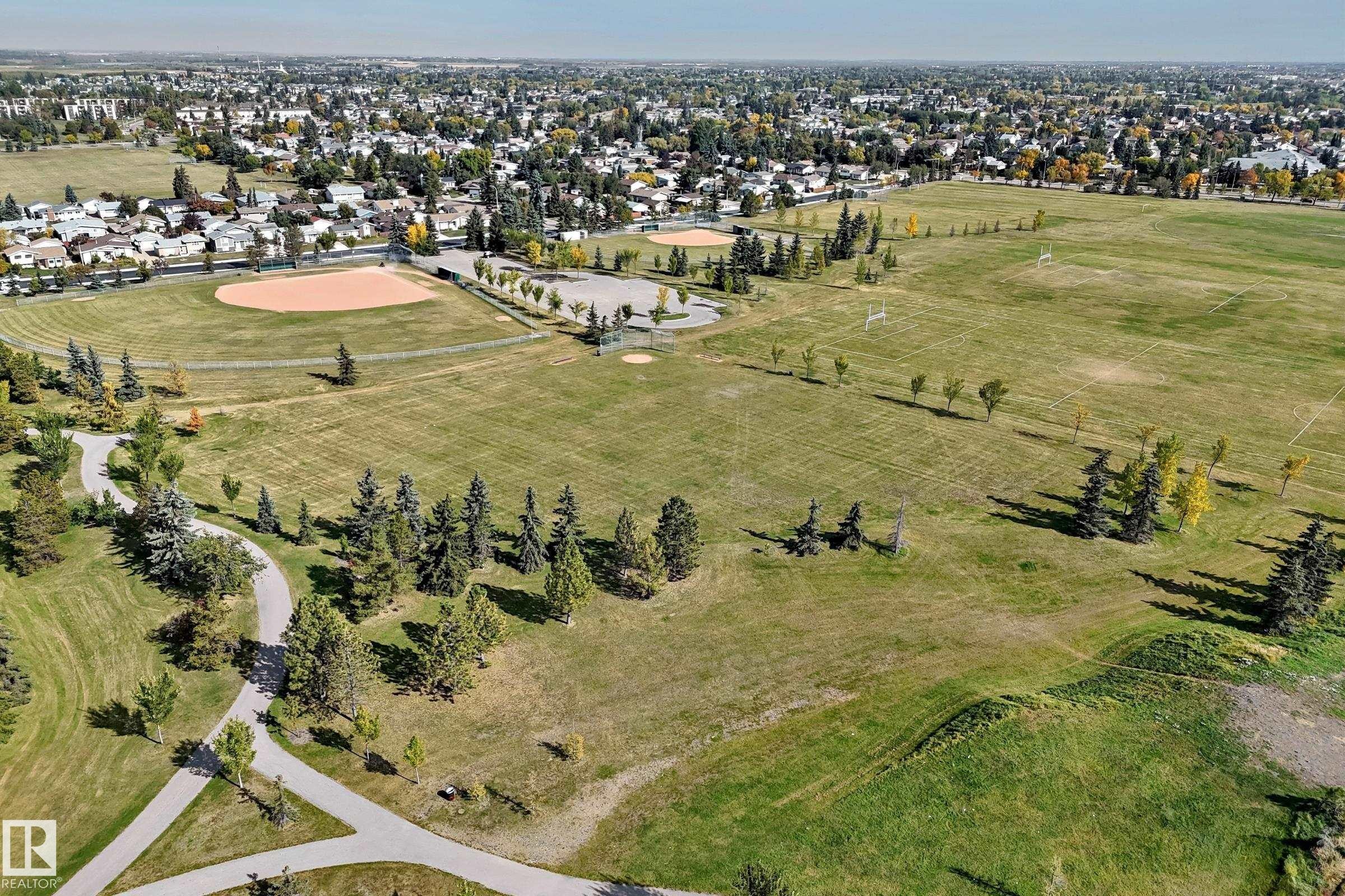 Expansive green space featuring recreational fields, mature trees, paved walking paths, and a distant residential backdrop - 161 Lancaster Terrace Nw, Edmonton, AB