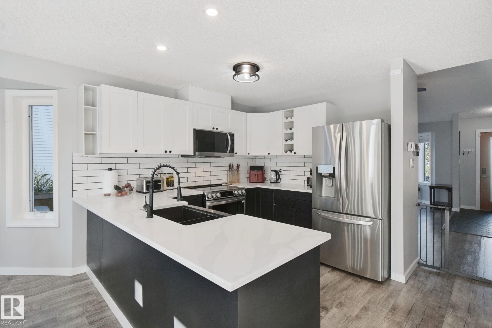 Modern kitchen with white and black cabinetry, white countertops, subway tile backsplash, and stainless steel appliances - 38 Menalta Place, Cardiff, AB