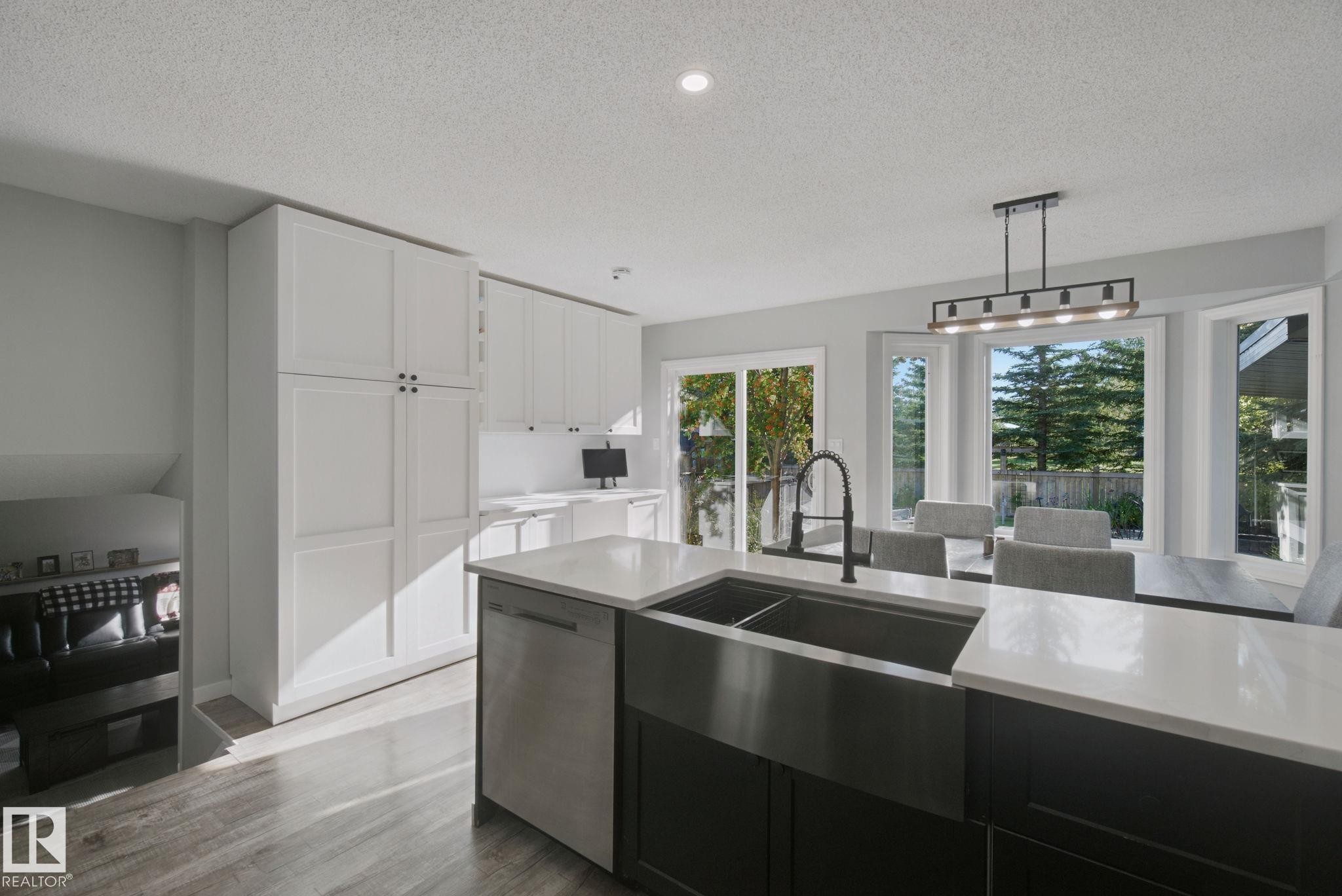 Spacious kitchen featuring white cabinetry, a large kitchen island with a dark basin sink, stainless steel dishwasher, and light countertops - 38 Menalta Place, Cardiff, AB