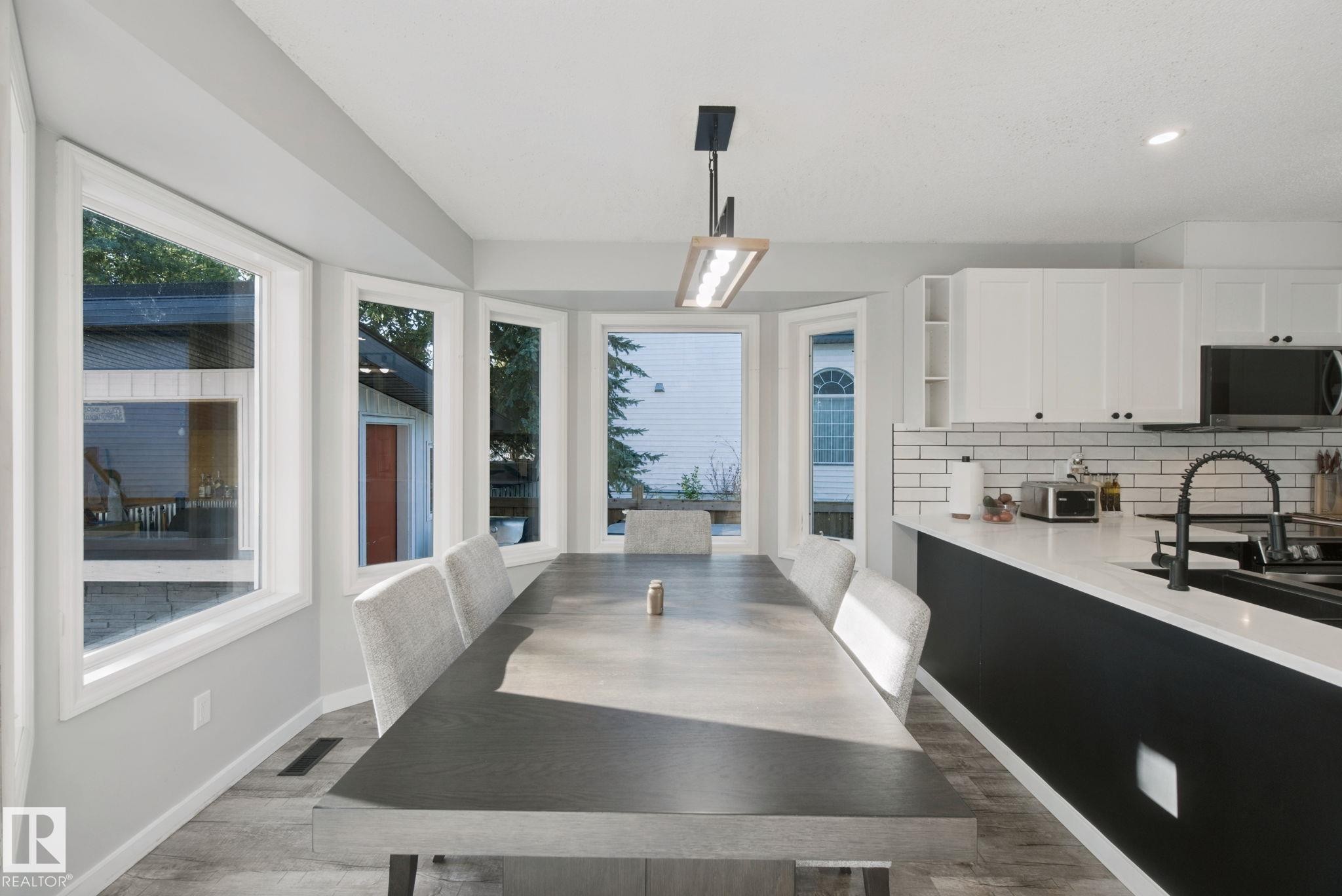 Open-concept kitchen and dining area featuring a modern black kitchen island, white upper cabinetry, subway tile backsplash, and light wood-finish flooring - 38 Menalta Place, Cardiff, AB