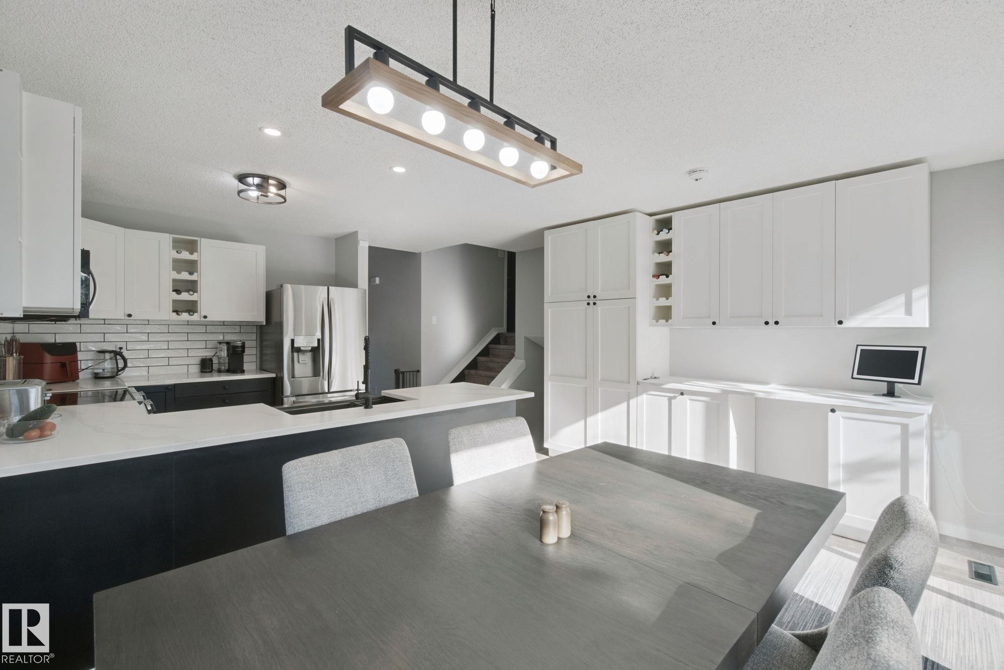Kitchen featuring white upper cabinetry, dark lower cabinetry, stainless steel appliances, and a subway tile backsplash - 38 Menalta Place, Cardiff, AB