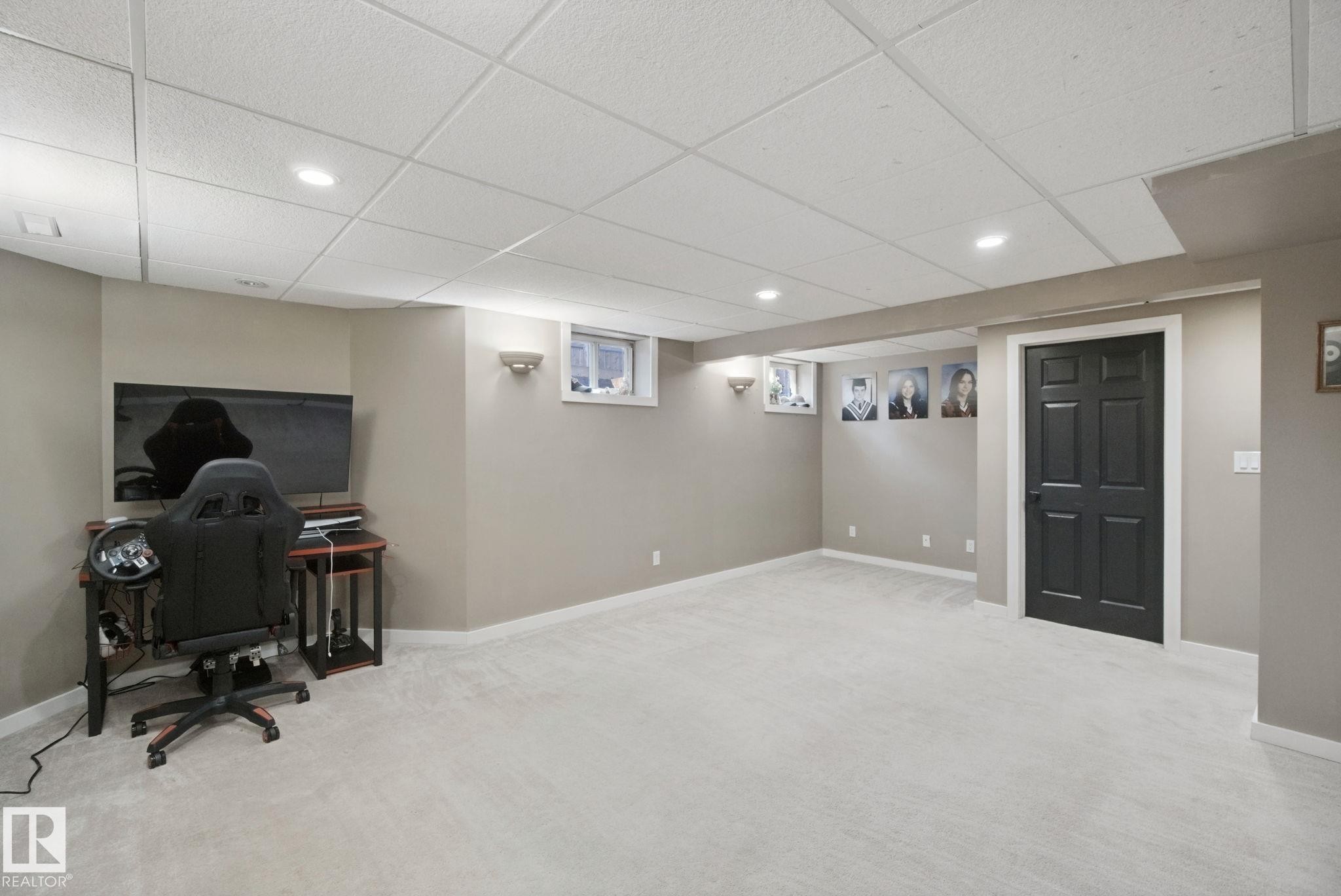Recessed lighting with sconce accents, neutral wall color, light-toned carpet flooring, drop ceiling, and a dark paneled door - 38 Menalta Place, Cardiff, AB