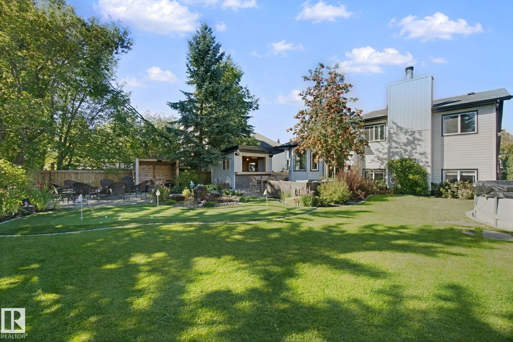 Expansive green lawn, putting green with multiple holes, established mature trees, stone patio area, and a wood privacy fence - 38 Menalta Place, Cardiff, AB