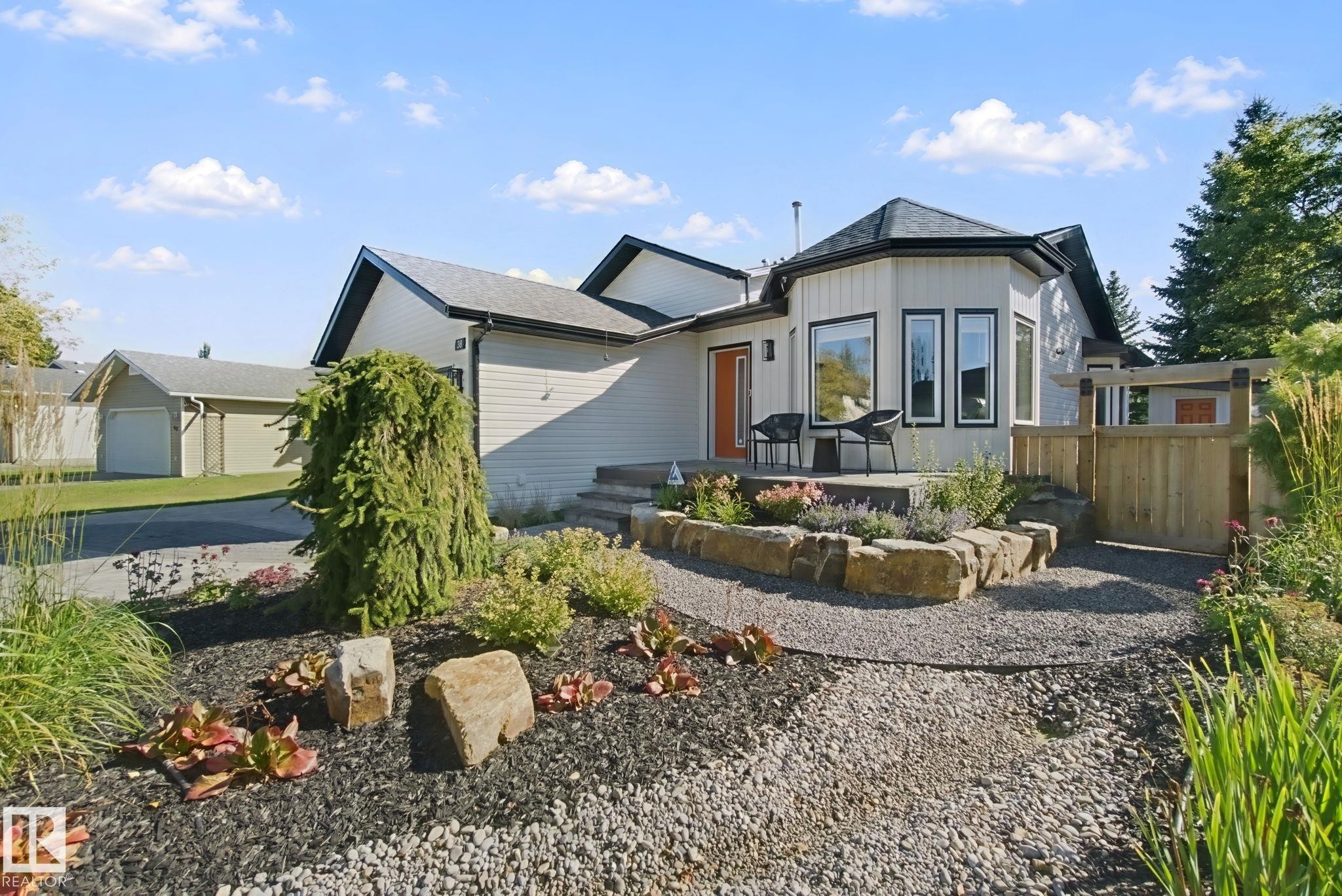 Exterior featuring a front patio, manicured landscaping with rock accents, gravel pathways, and an attached garage - 38 Menalta Place, Cardiff, AB