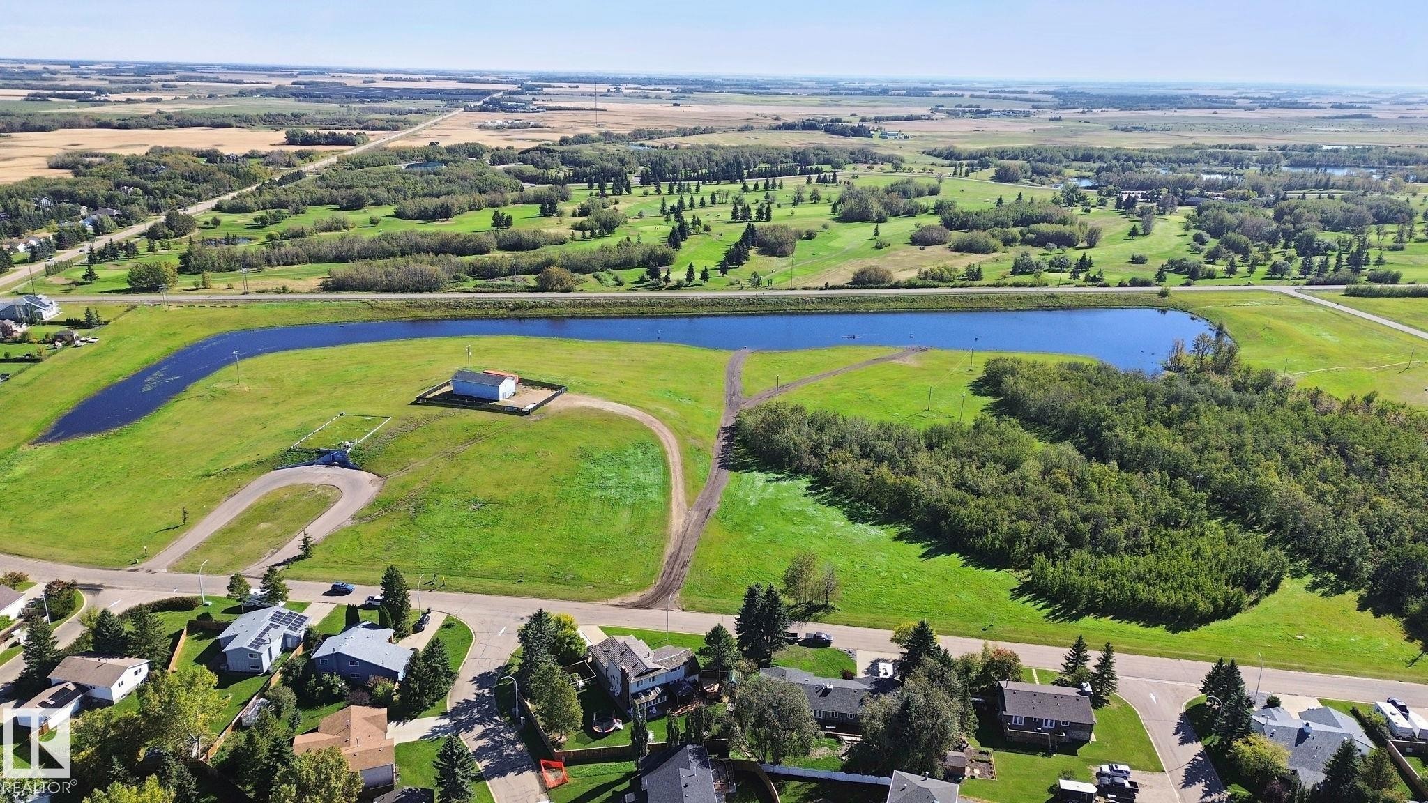 Expansive green space featuring a large pond, adjacent wooded areas, and surrounding cultivated fields - 38 Menalta Place, Cardiff, AB