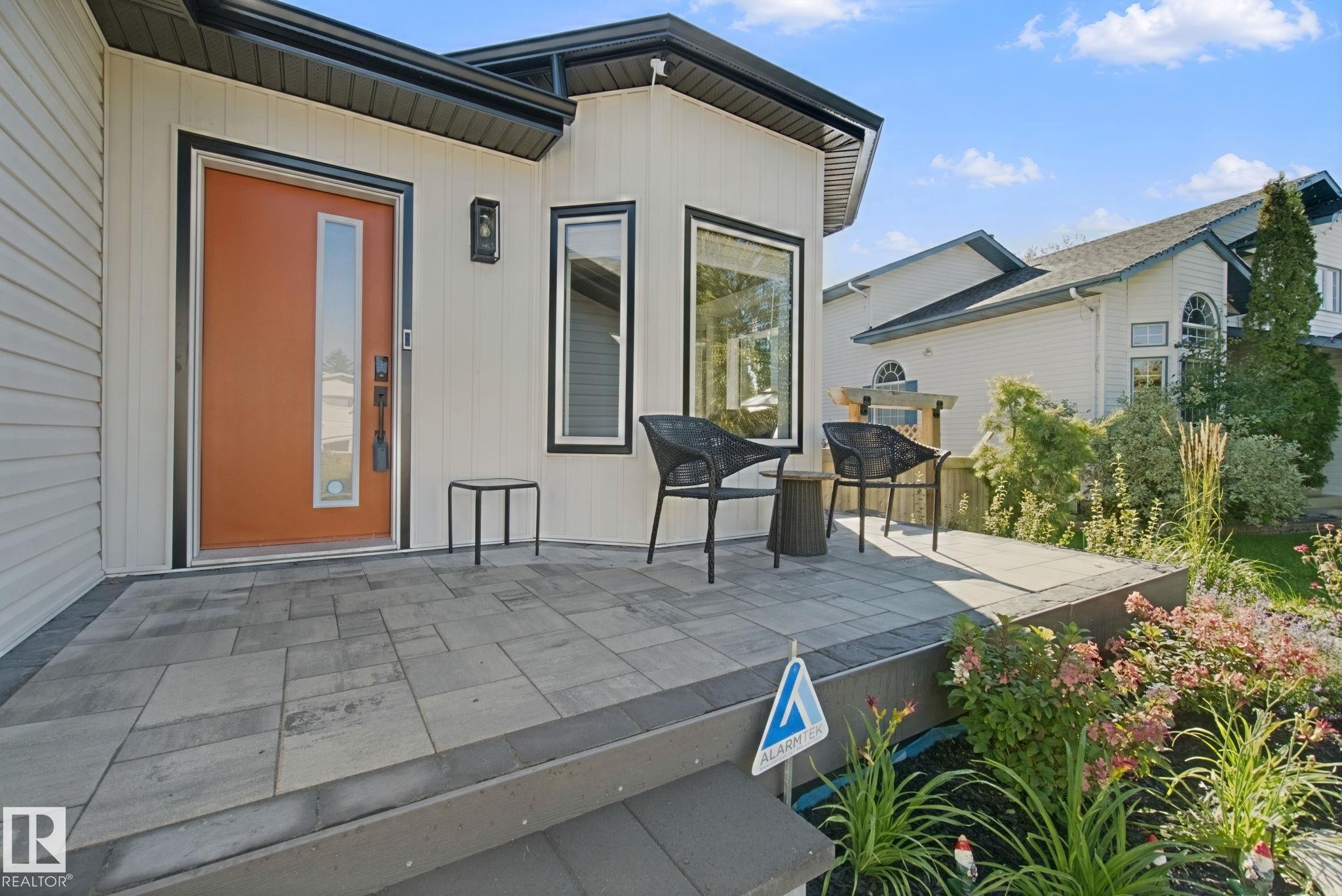 Inviting front entry with a vibrant orange door, rectangular transom window, and a modern exterior light fixture - 38 Menalta Place, Cardiff, AB