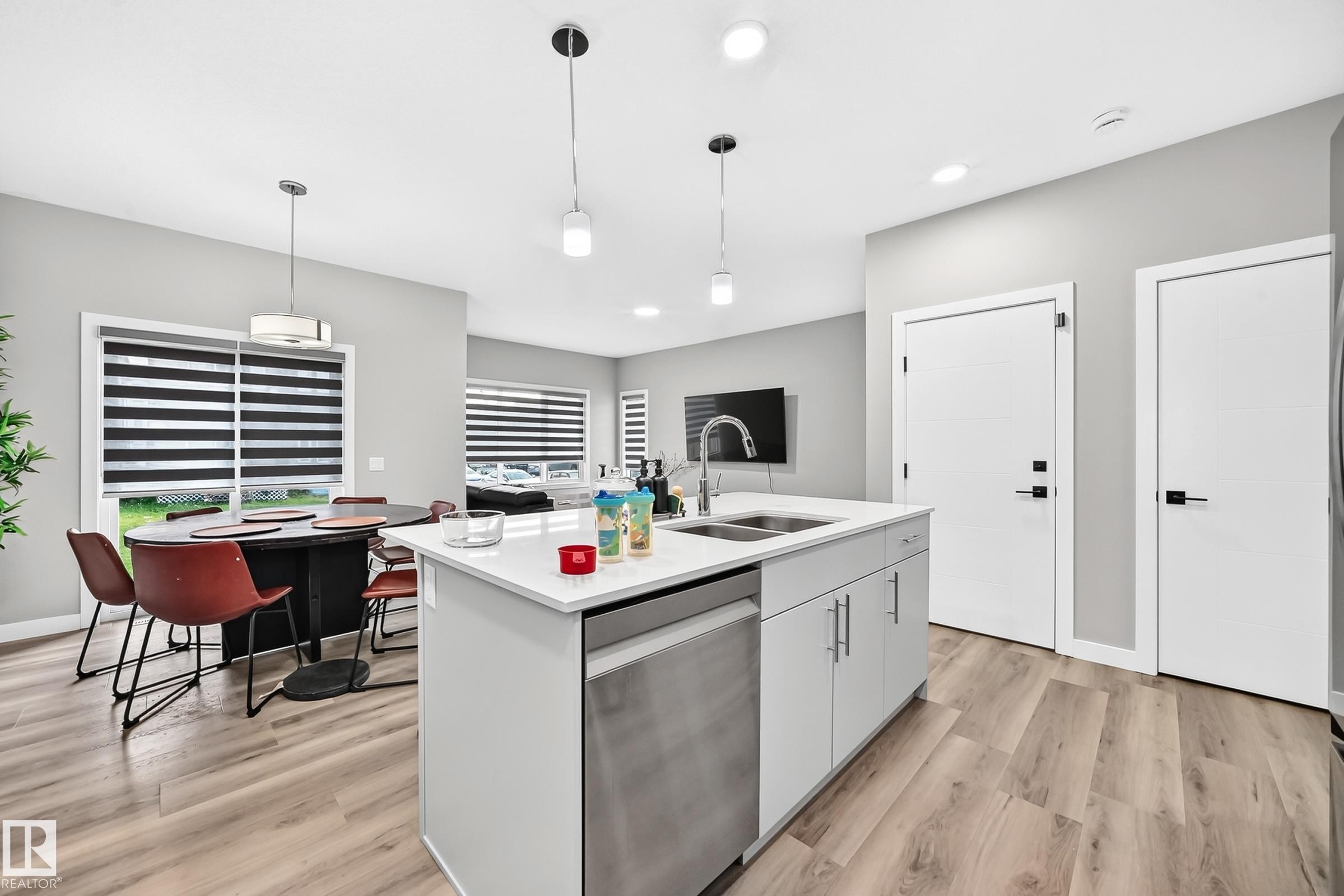 Kitchen island with integrated sink, stainless steel dishwasher, white shaker-style cabinetry, and light-toned wood-finish flooring - 2415 194 Street Nw, Edmonton, AB