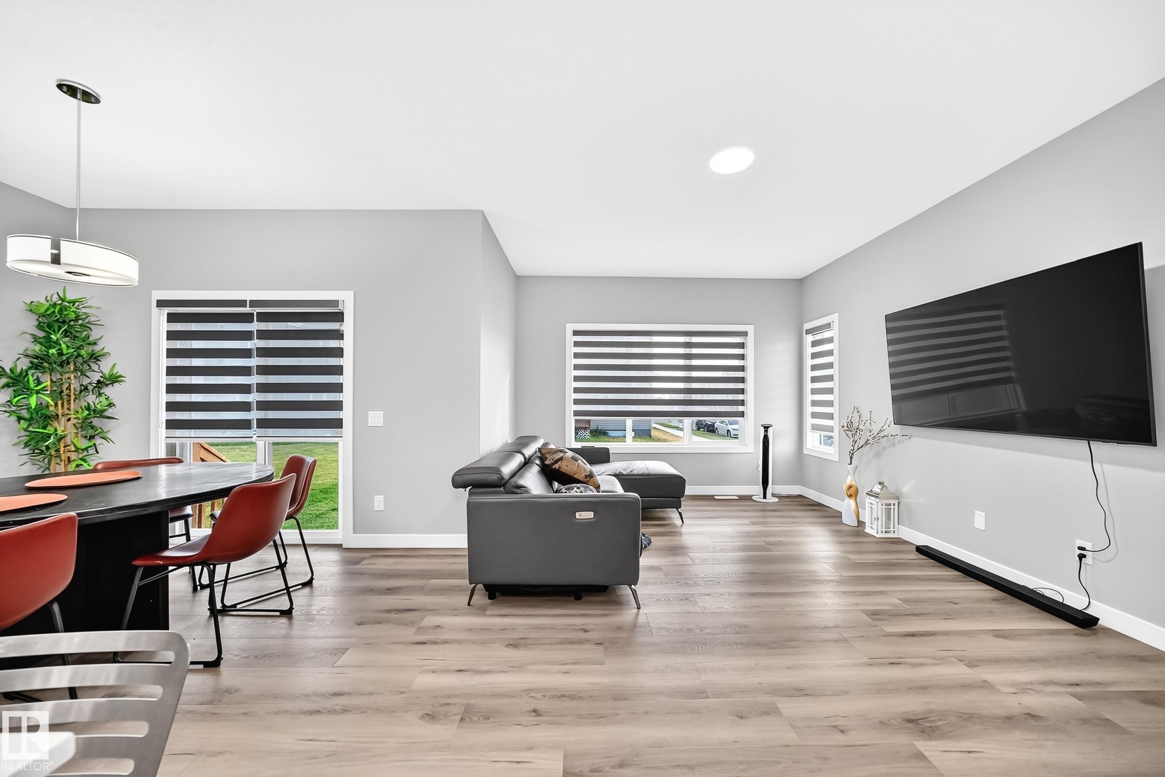 Spacious living area featuring wood-finish flooring, ample natural light, recessed ceiling lighting, and a modern dining pendant light - 2415 194 Street Nw, Edmonton, AB