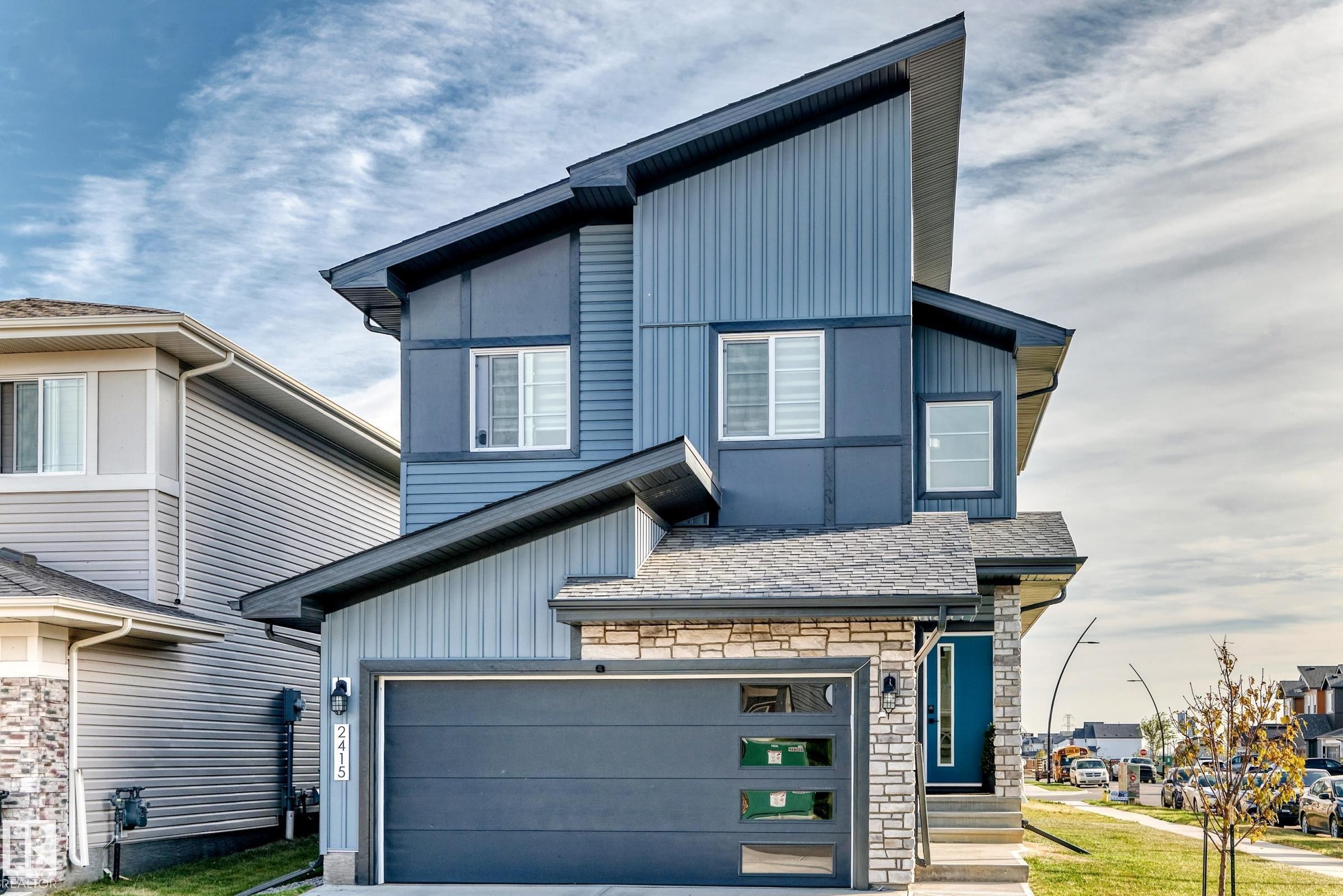 Modern architectural design with a multi-textured facade, stone accents, and a contrasting blue entry door - 2415 194 Street Nw, Edmonton, AB
