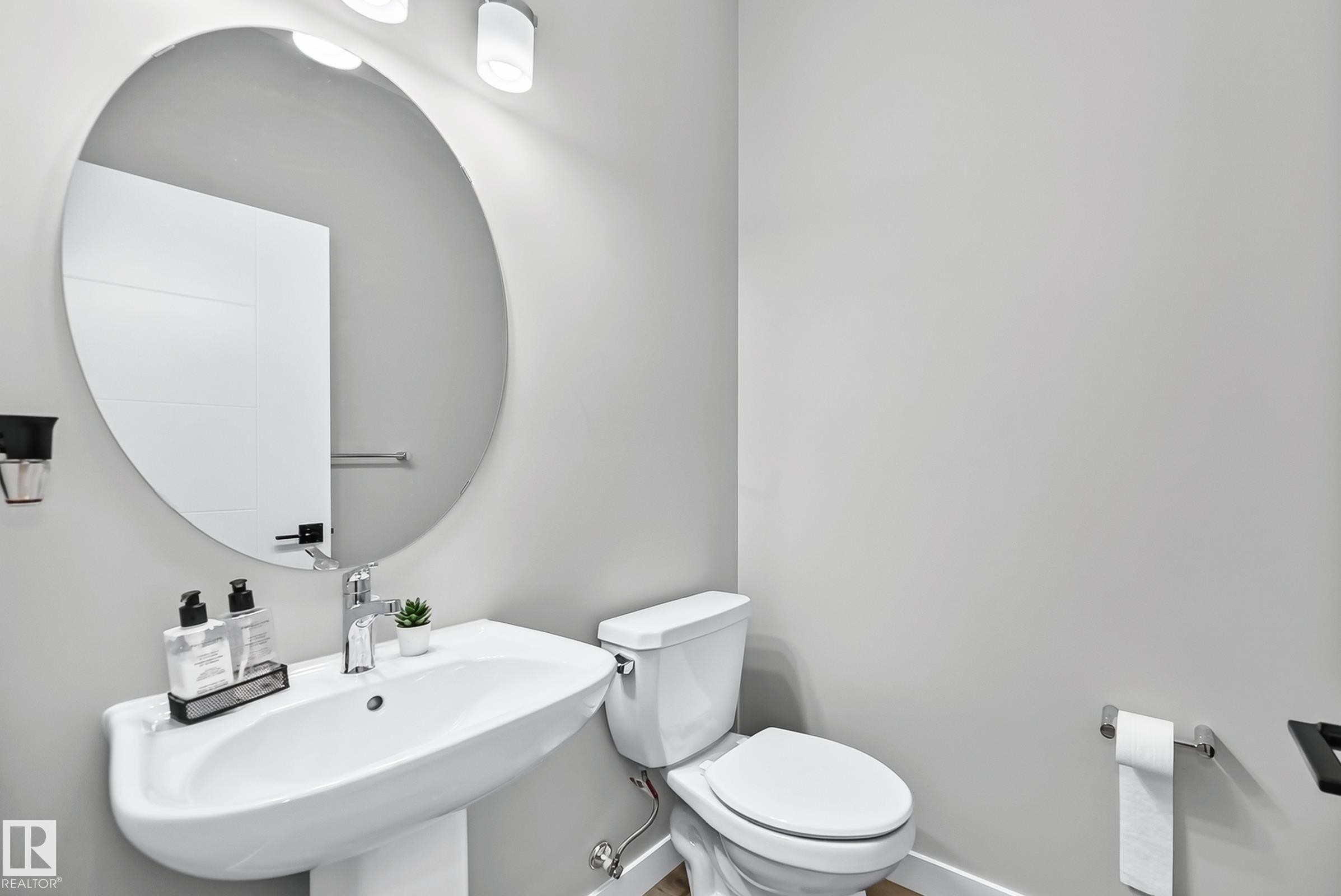 Pedestal sink with chrome faucet, circular wall-mounted mirror, and white toilet - 2415 194 Street Nw, Edmonton, AB