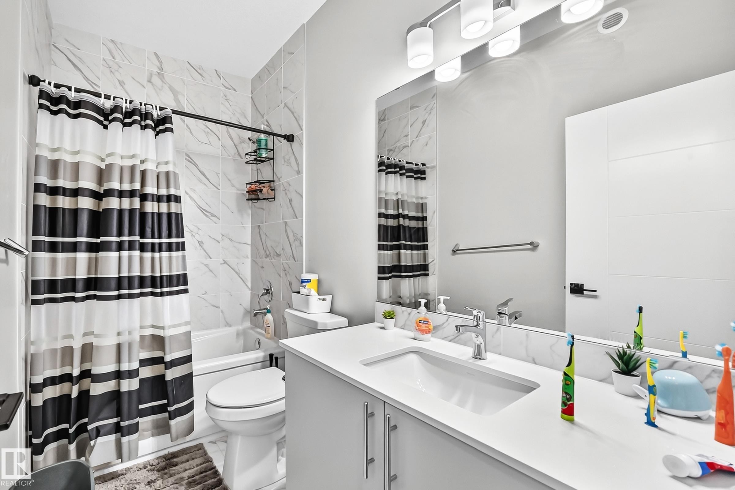 Modern bathroom featuring a single vanity with a white countertop and undermount sink, a large wall mirror, and a built-in bathtub with subway tile surround - 2415 194 Street Nw, Edmonton, AB