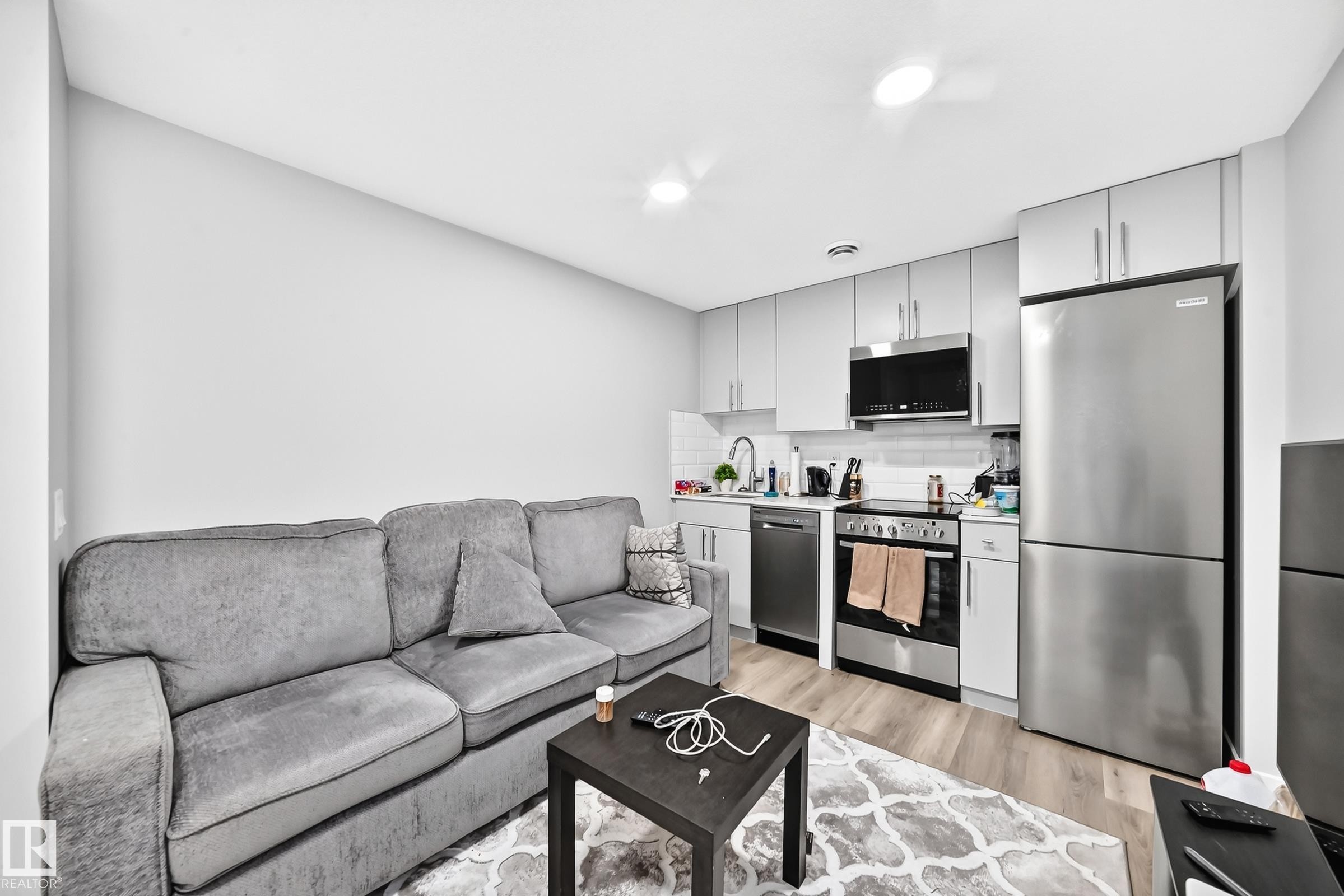 Galley kitchen with light gray cabinetry, stainless steel appliances, white subway tile backsplash, and wood-finish flooring - 2415 194 Street Nw, Edmonton, AB