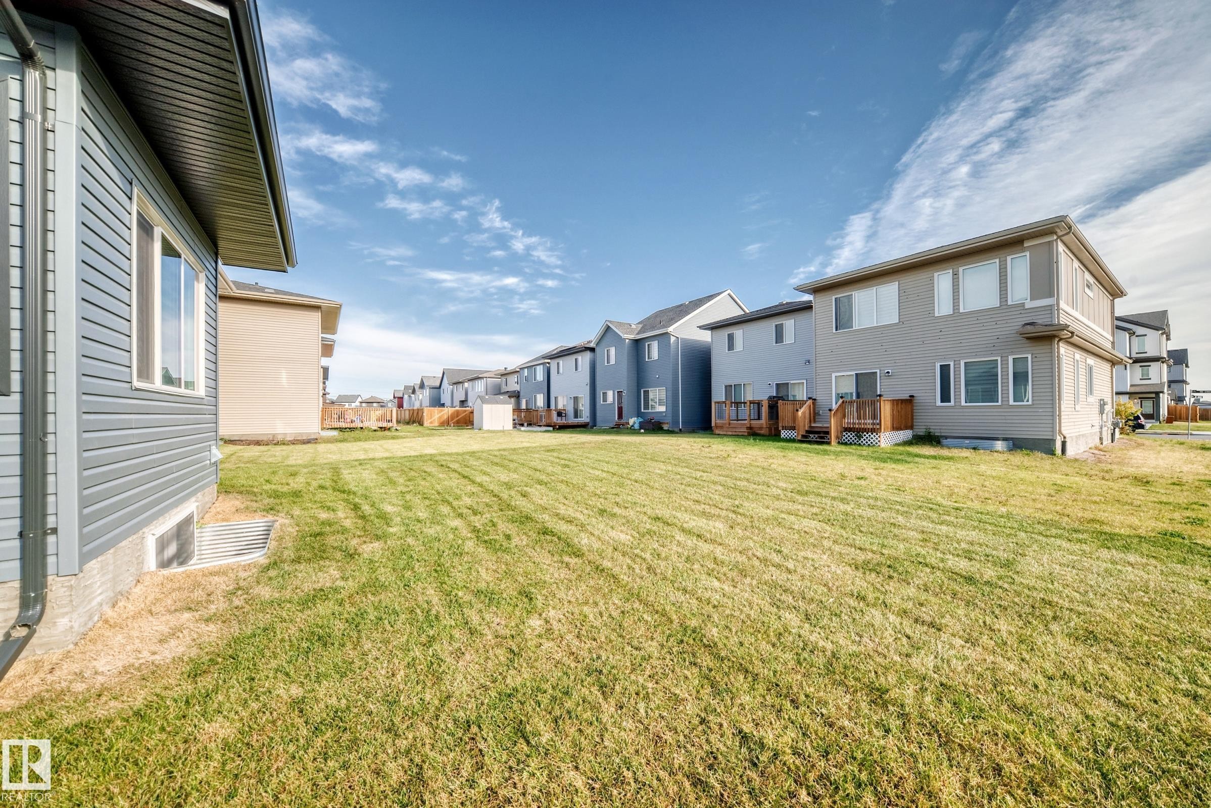 Expansive grass lawn with a row of properties featuring wood decks - 2415 194 Street Nw, Edmonton, AB