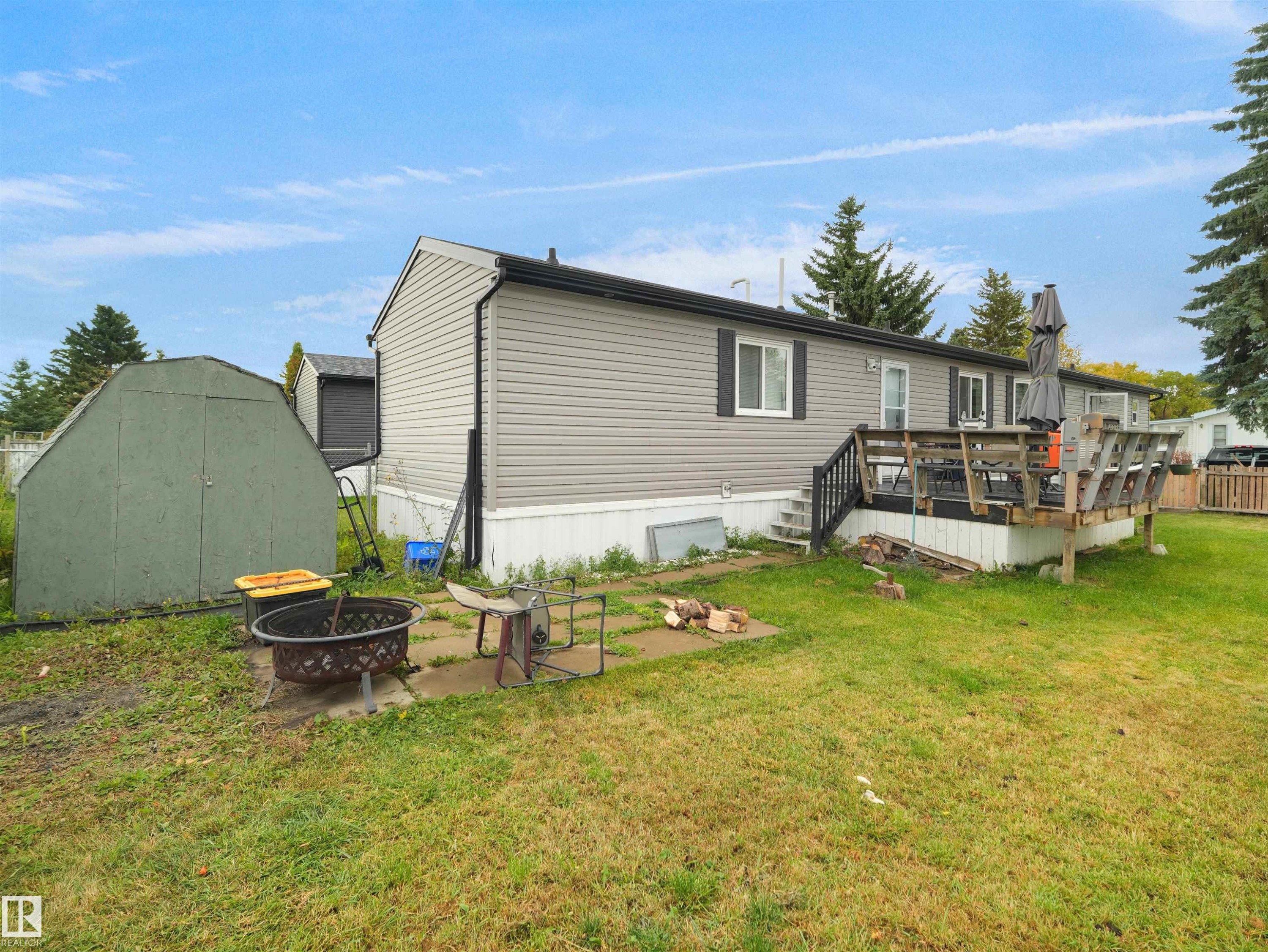 Rear exterior showcasing gray horizontal siding, a wooden deck with dark railing, and a green storage shed - 52 Evergreen Park Northwest, Edmonton, AB