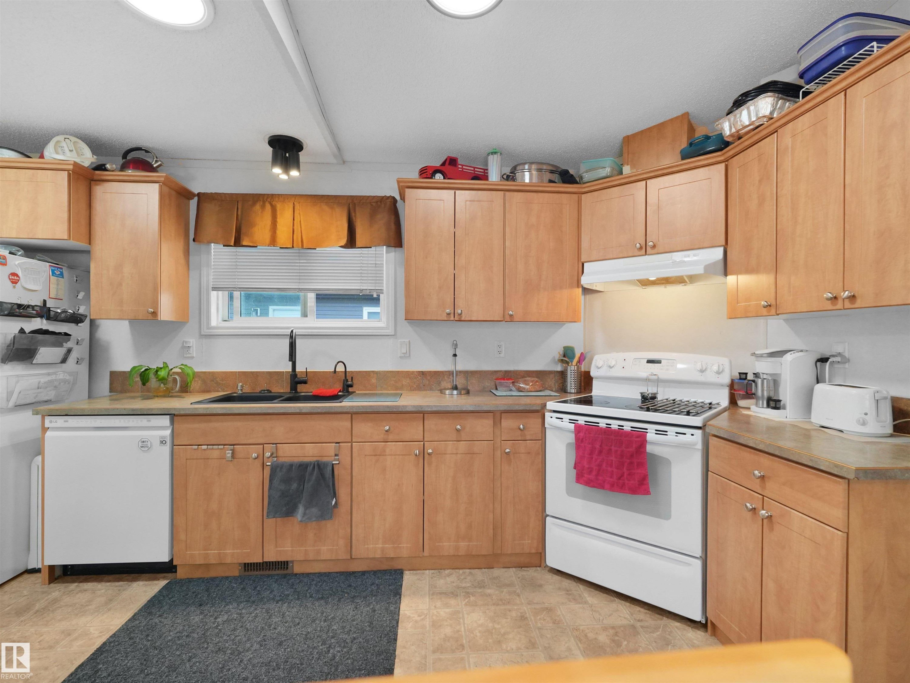 Light wood-finish cabinetry, solid surface countertops, a stainless steel sink with a matte black faucet, and white appliances - 52 Evergreen Park Northwest, Edmonton, AB