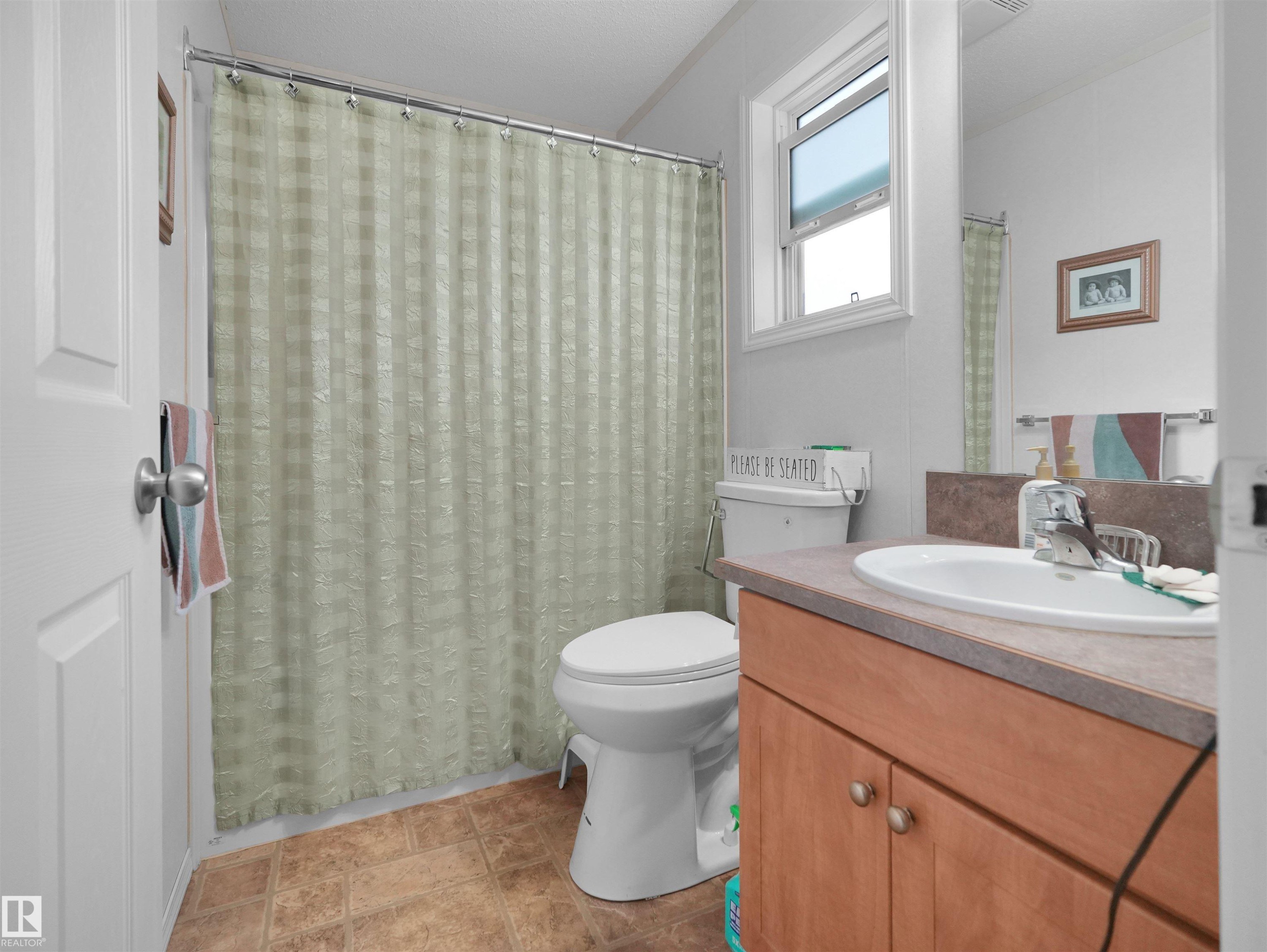 Bathroom featuring a vanity with a white basin sink, wood-finish cabinetry, and a window - 52 Evergreen Park Northwest, Edmonton, AB