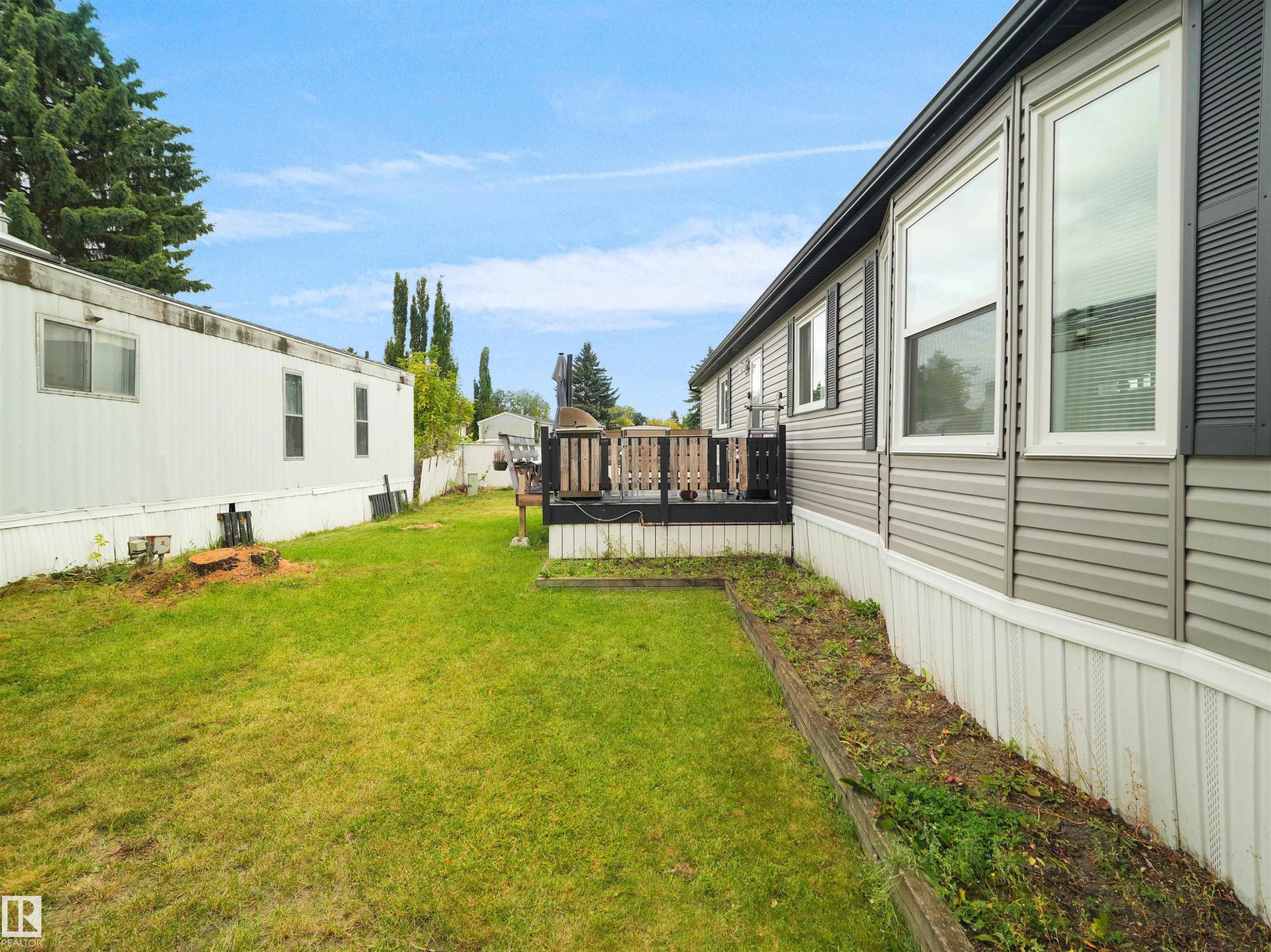 Expansive green lawn, raised wooden garden bed, dark wood deck with railing, and gray vinyl siding - 52 Evergreen Park Northwest, Edmonton, AB