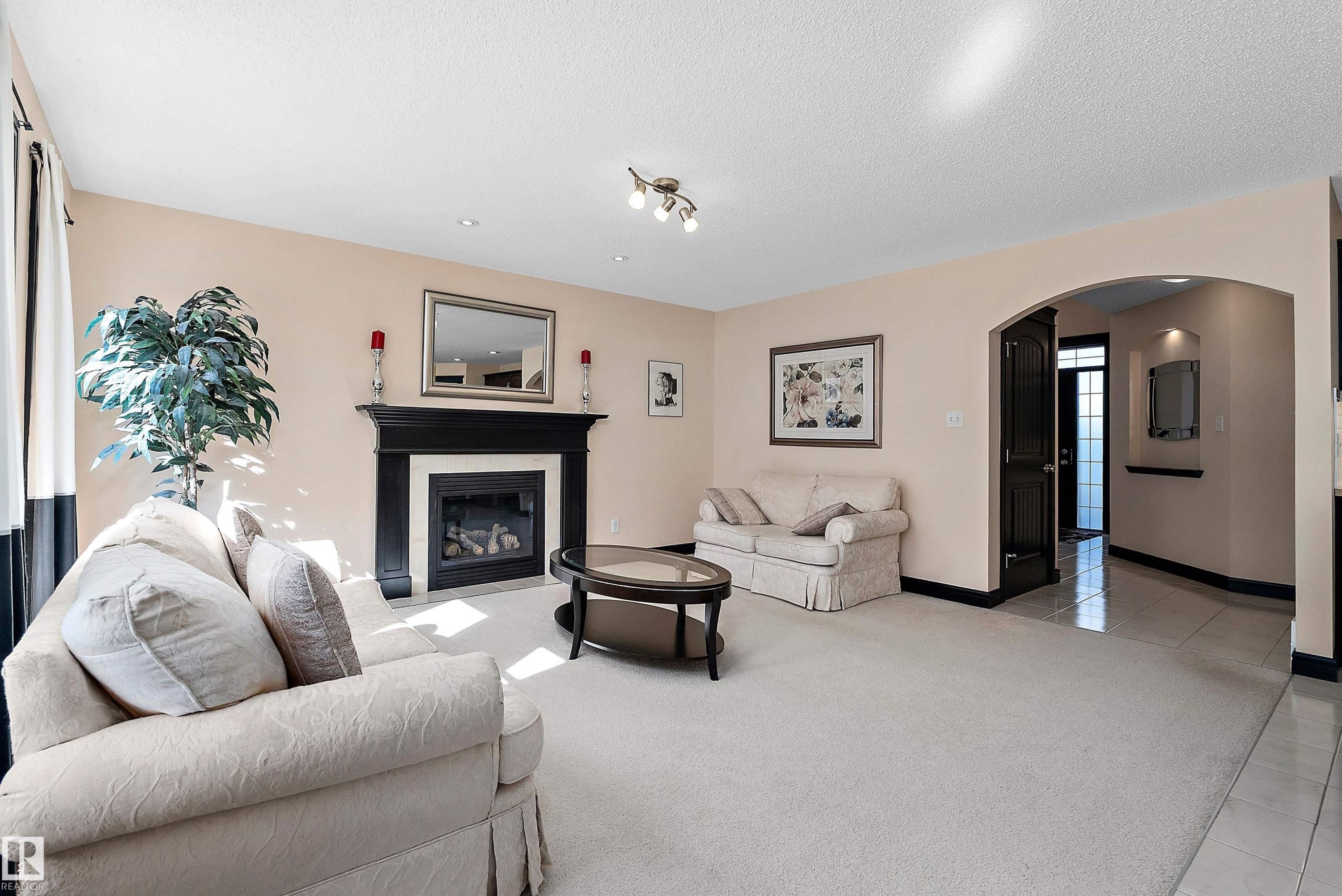 Carpeted living area with a fireplace featuring a black mantel, recessed lighting, and an arched doorway - 11515 16 Avenue Sw, Edmonton, AB