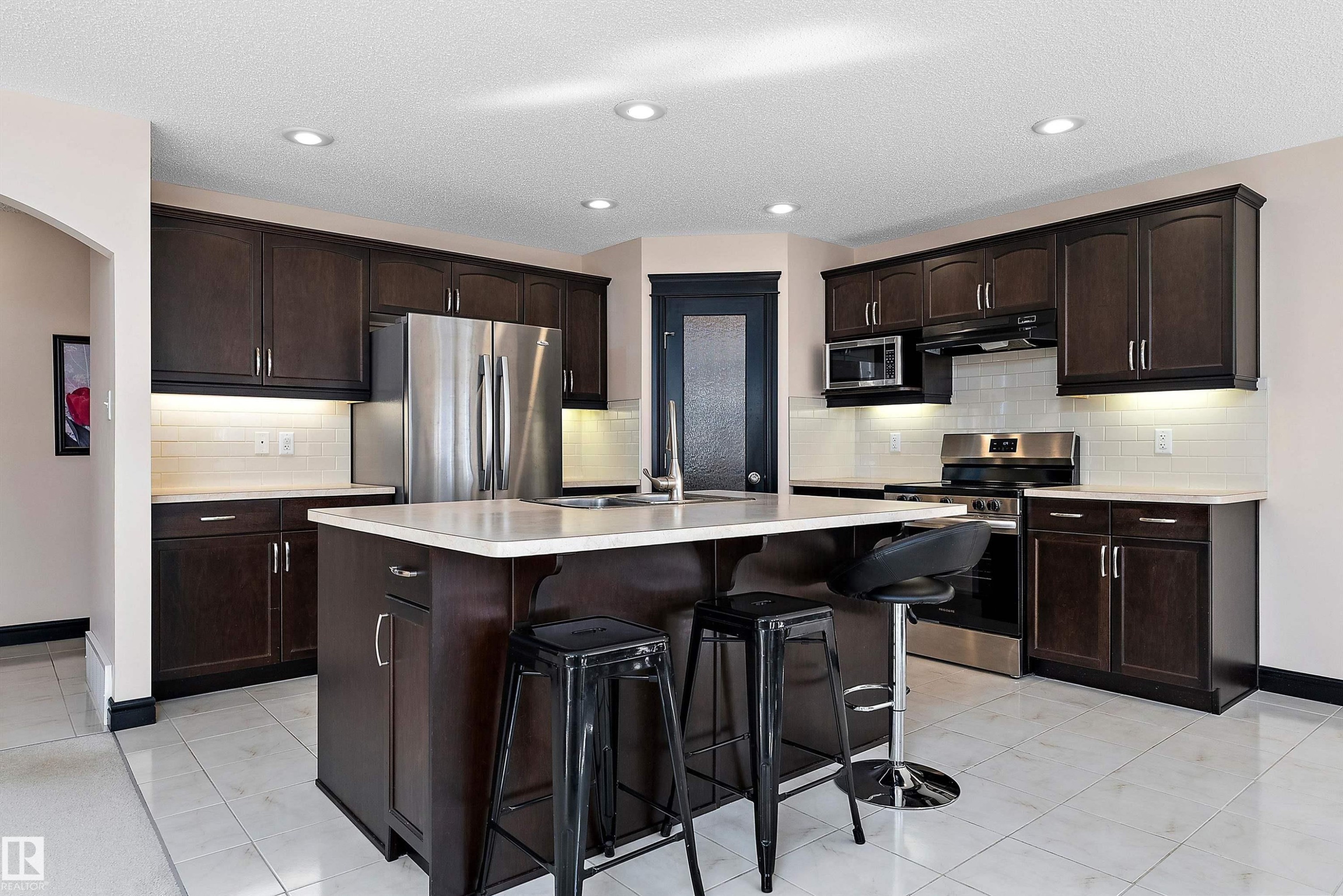 Kitchen featuring dark wood-finish cabinetry, stainless steel appliances, a central island with countertop, tiled flooring, and recessed lighting - 11515 16 Avenue Sw, Edmonton, AB