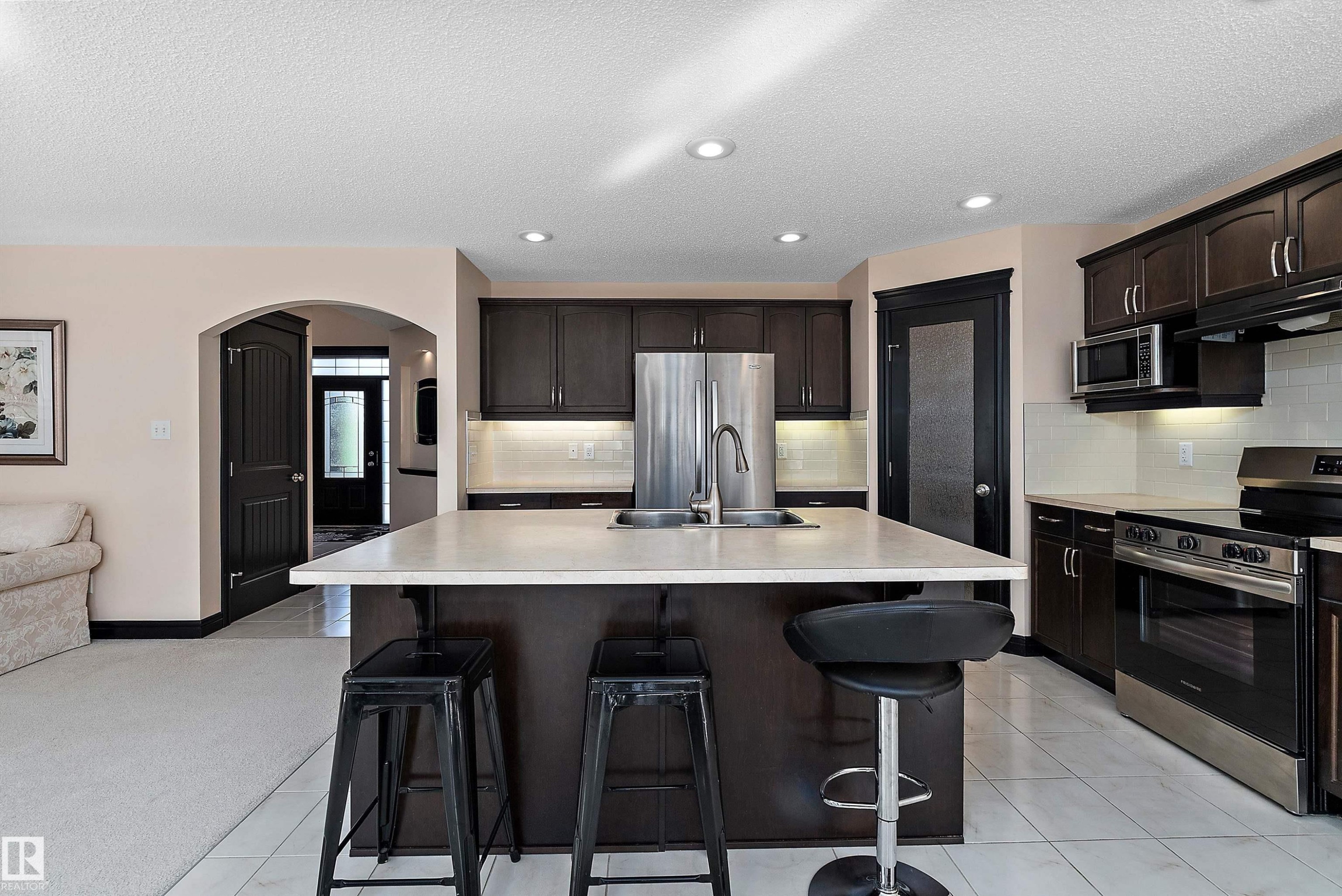 Kitchen featuring a central island with an undermount sink, dark wood cabinetry, stainless steel appliances, and tile flooring - 11515 16 Avenue Sw, Edmonton, AB