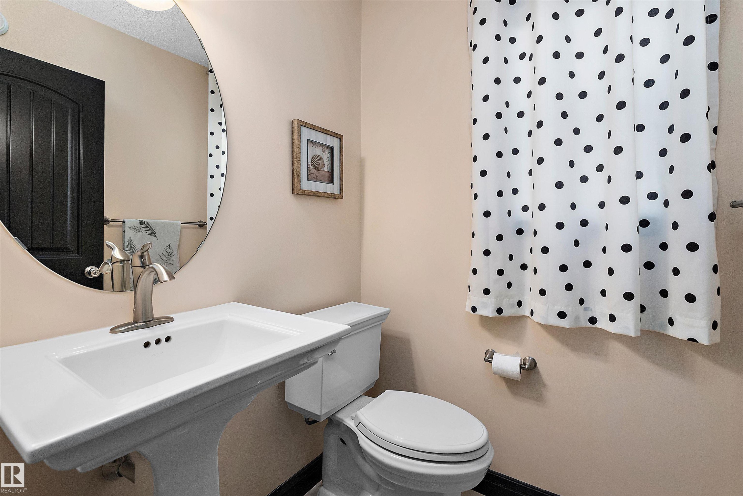 Pedestal sink with a brushed nickel faucet, round wall-mounted mirror, and a white toilet - 11515 16 Avenue Sw, Edmonton, AB