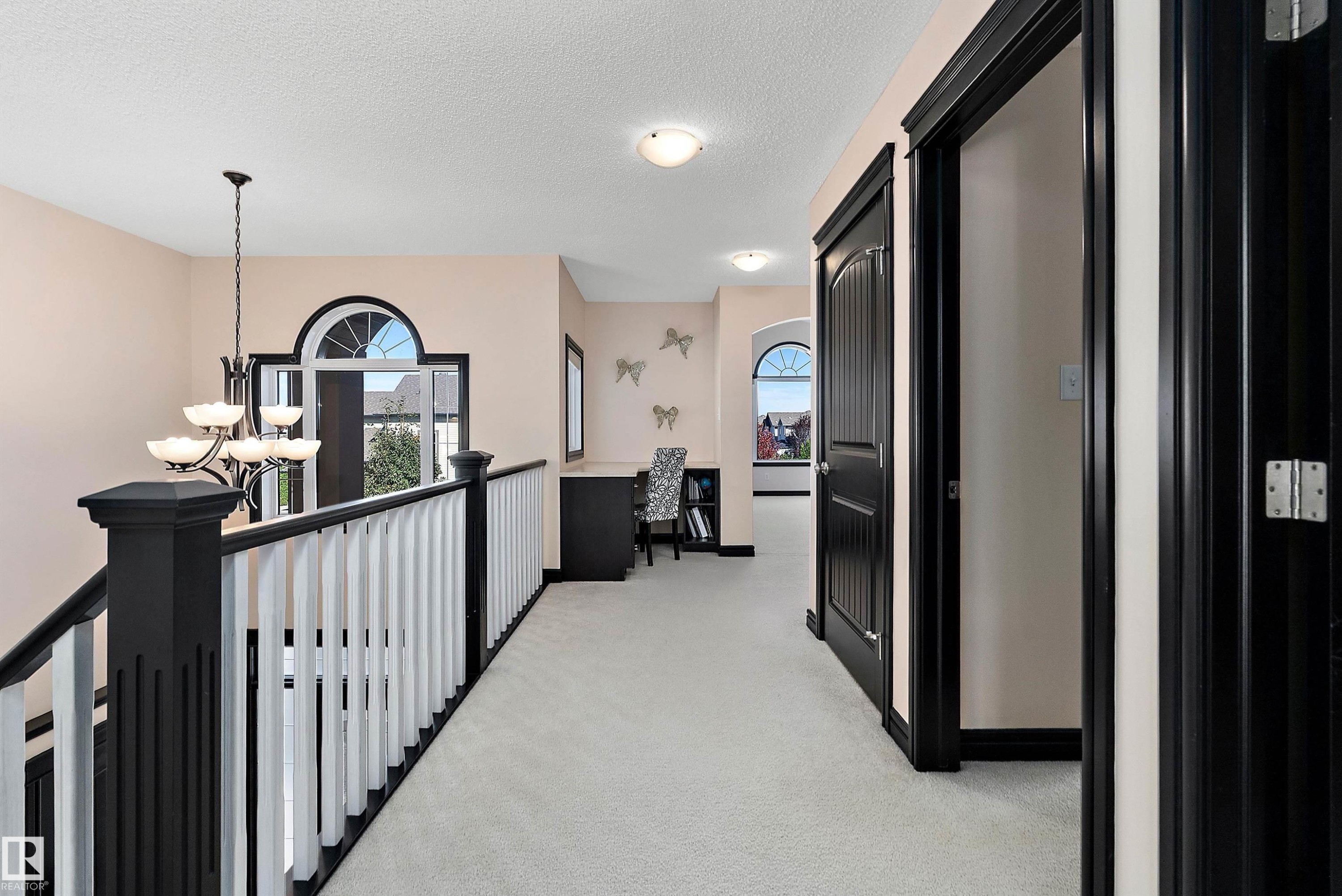 Open hallway with carpet flooring, a chandelier, and a black and white staircase railing - 11515 16 Avenue Sw, Edmonton, AB