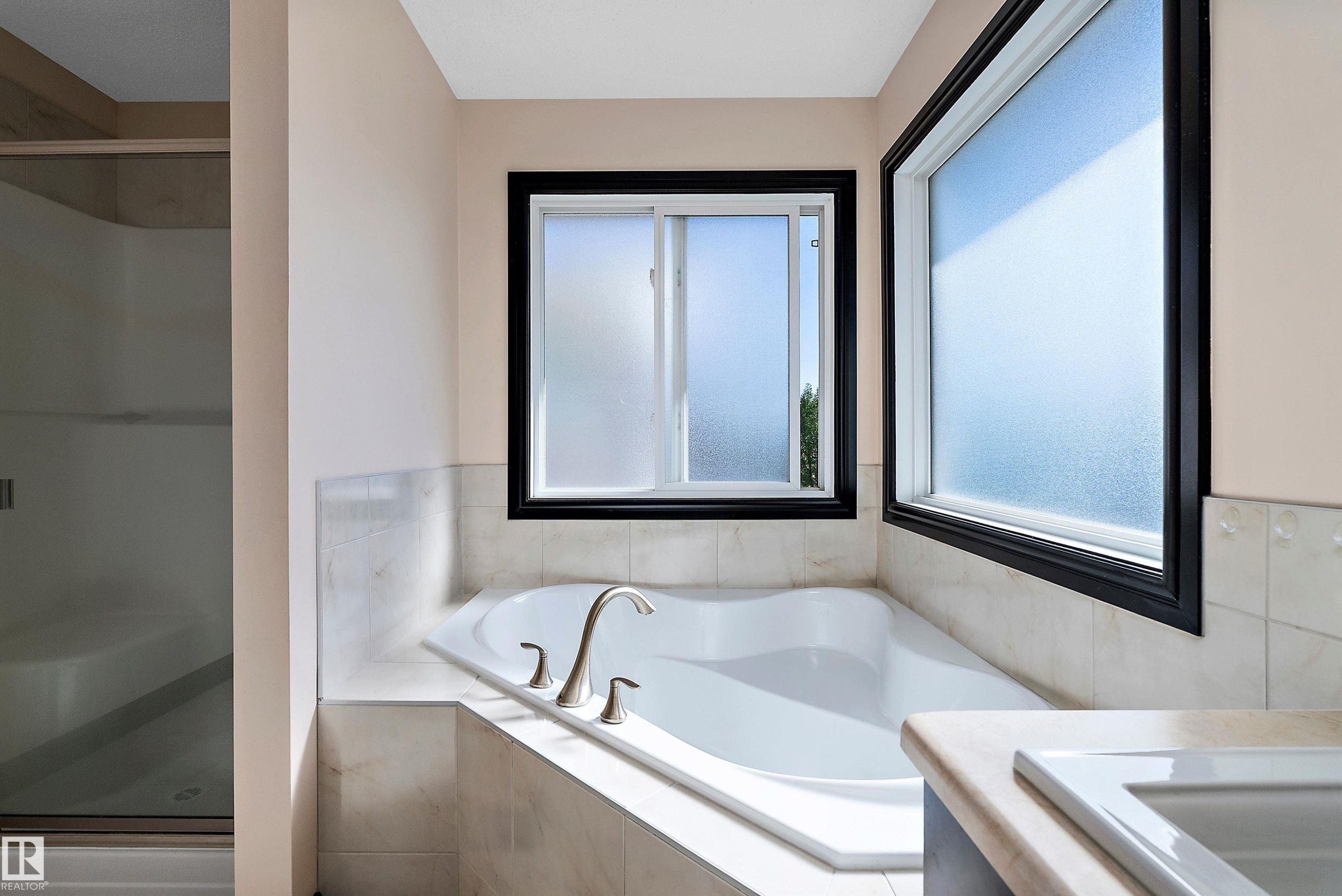 Built-in soaking tub with brushed nickel fixtures, tiled surround, and two opaque windows - 11515 16 Avenue Sw, Edmonton, AB