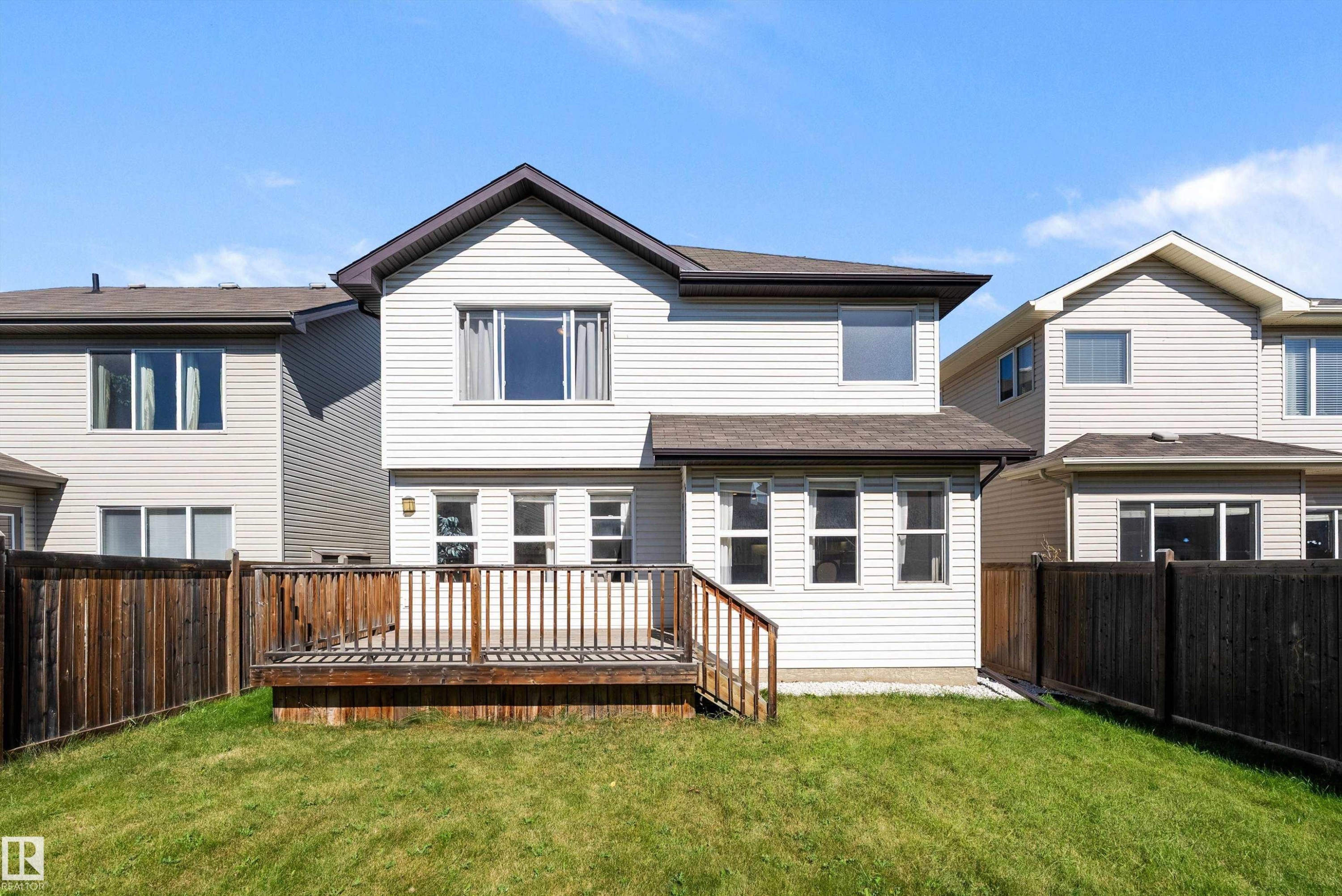 Spacious backyard featuring a wooden deck with railing, a grassy lawn, and horizontal privacy fencing - 11515 16 Avenue Sw, Edmonton, AB