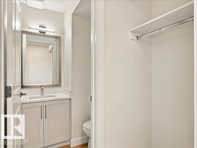 White vanity with brushed nickel hardware, quartz countertop, undermount sink, wall-mounted light fixture, and framed mirror - 18325 66 Avenue Nw, Edmonton, AB