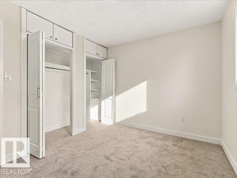 Wall-to-wall carpeting with built-in closets featuring bi-fold doors, hanging rods, and overhead cabinetry - 18325 66 Avenue Nw, Edmonton, AB