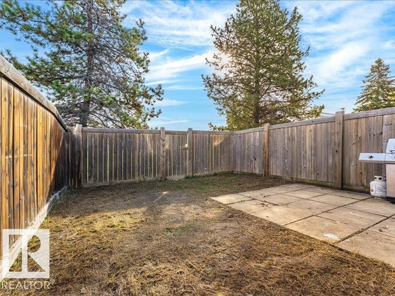 Enclosed outdoor area featuring wood fencing, a paved patio, and mature trees - 18325 66 Avenue Nw, Edmonton, AB