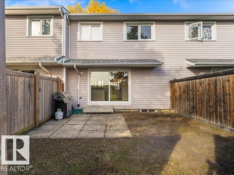 Fenced backyard with a concrete patio, sliding glass door, and upper-level windows - 18325 66 Avenue Nw, Edmonton, AB