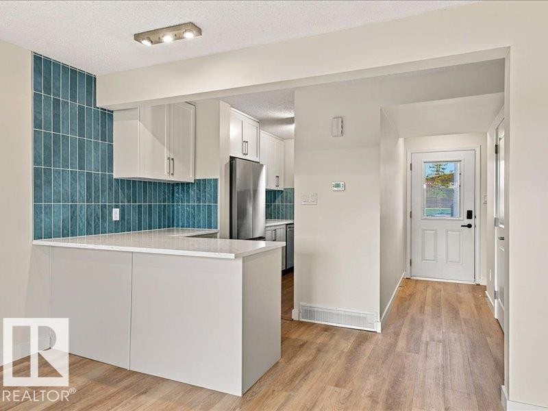 Breakfast bar with white countertop, subway tile backsplash, wood-finish flooring, white cabinetry, and stainless steel refrigerator - 18325 66 Avenue Nw, Edmonton, AB