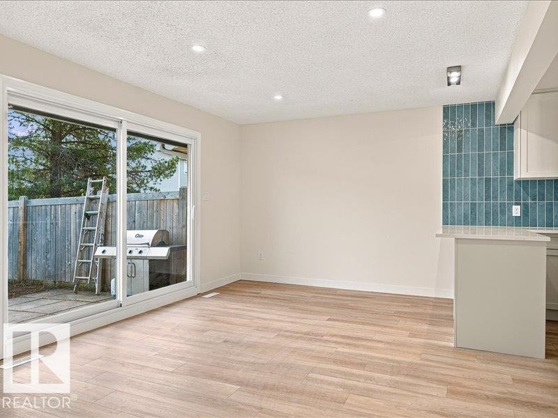 Wood-finish flooring throughout, recessed ceiling lighting, a turquoise tile backsplash, and a sliding glass door to the exterior - 18325 66 Avenue Nw, Edmonton, AB