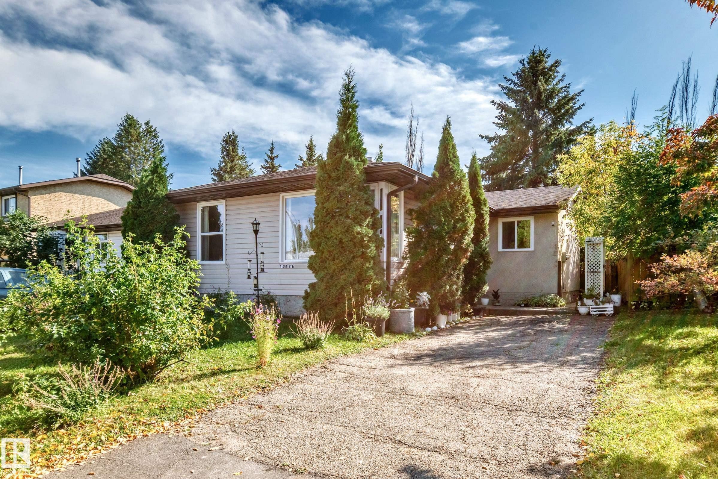 Siding exterior with a pitched roof, front garden with mature shrubs and trees, and a paved driveway - 11007 173A Avenue Nw, Edmonton, AB